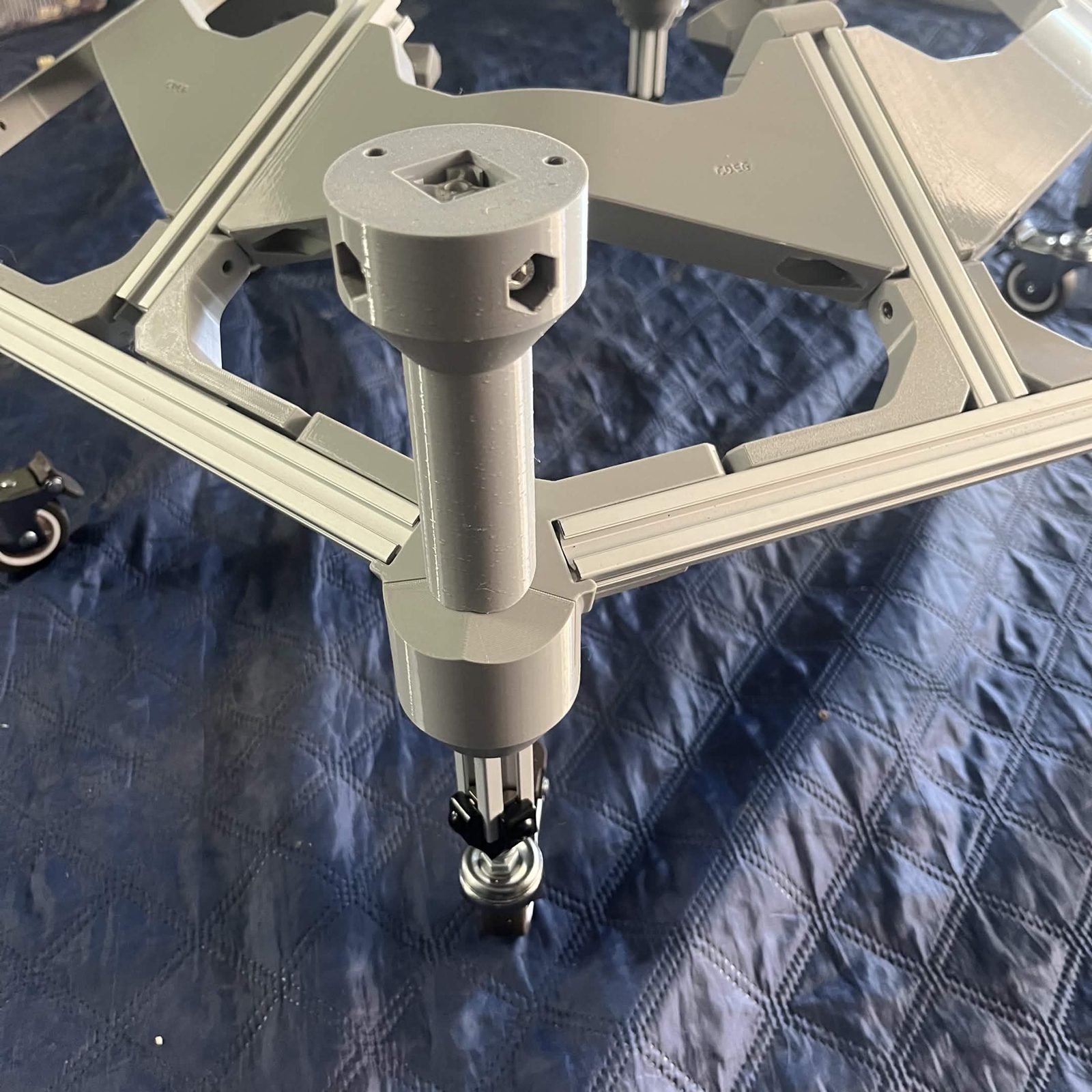 One corner of the bottom layer seen close up from above: the External bracket — bottom vertical standing on the collar with the end of piece D recessed in its square socket, the foot cover below the frame, and the caster under that