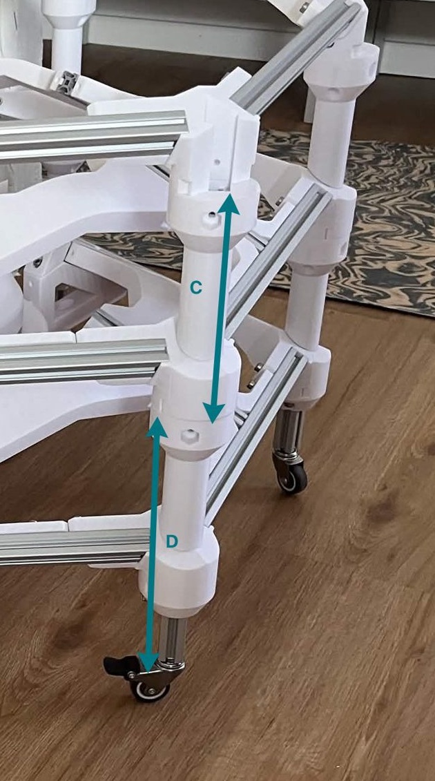 One corner of a built machine close up, with the C layer vertical support marked by an arrow between the two frames above and the longer D foot extension marked by an arrow running from the caster up past the bottom frame to the second