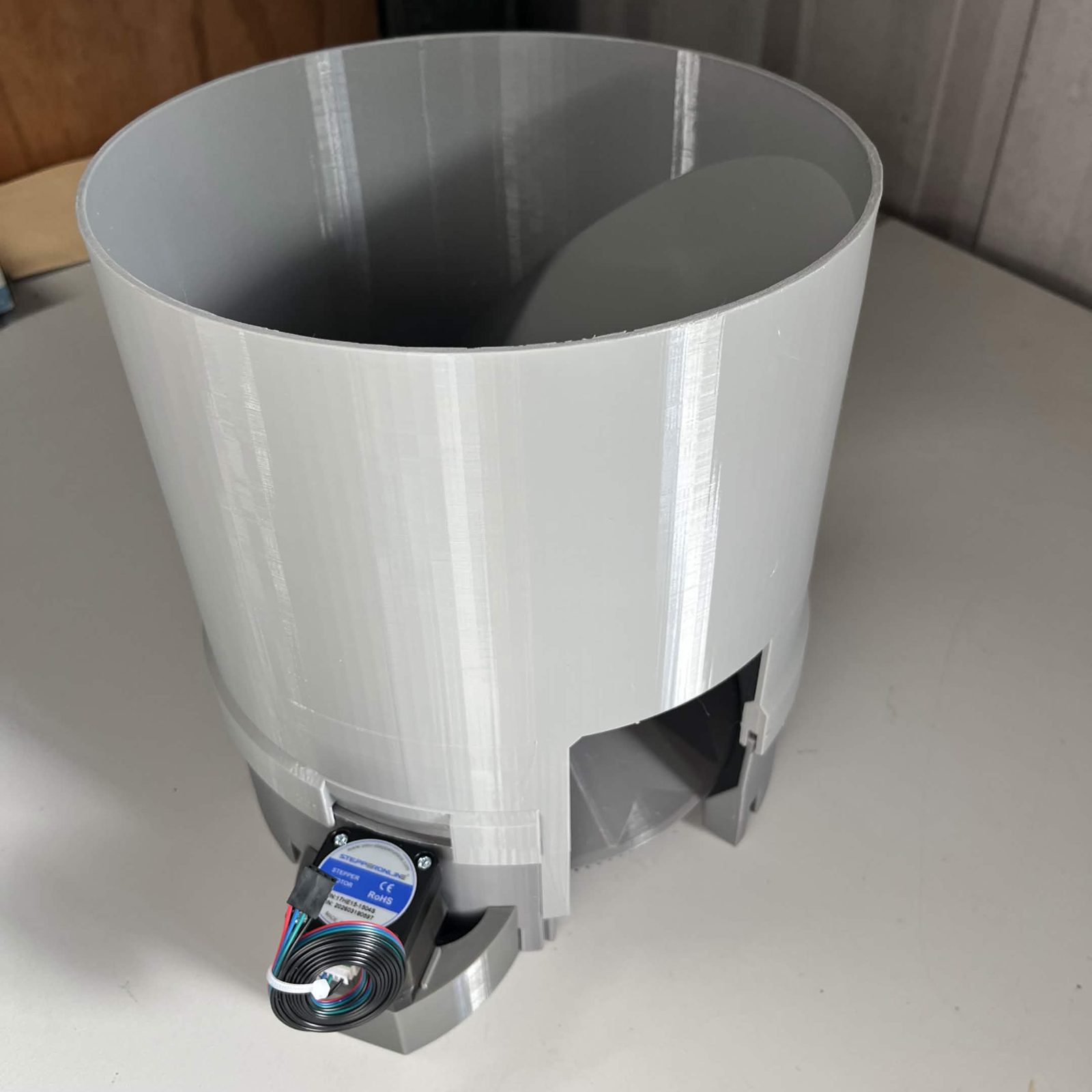 A finished C1 on the bench: the tall cylindrical bulk cap seated on the channel below it, its outlet opening at the front right, the stepper motor at the front with its lead coiled