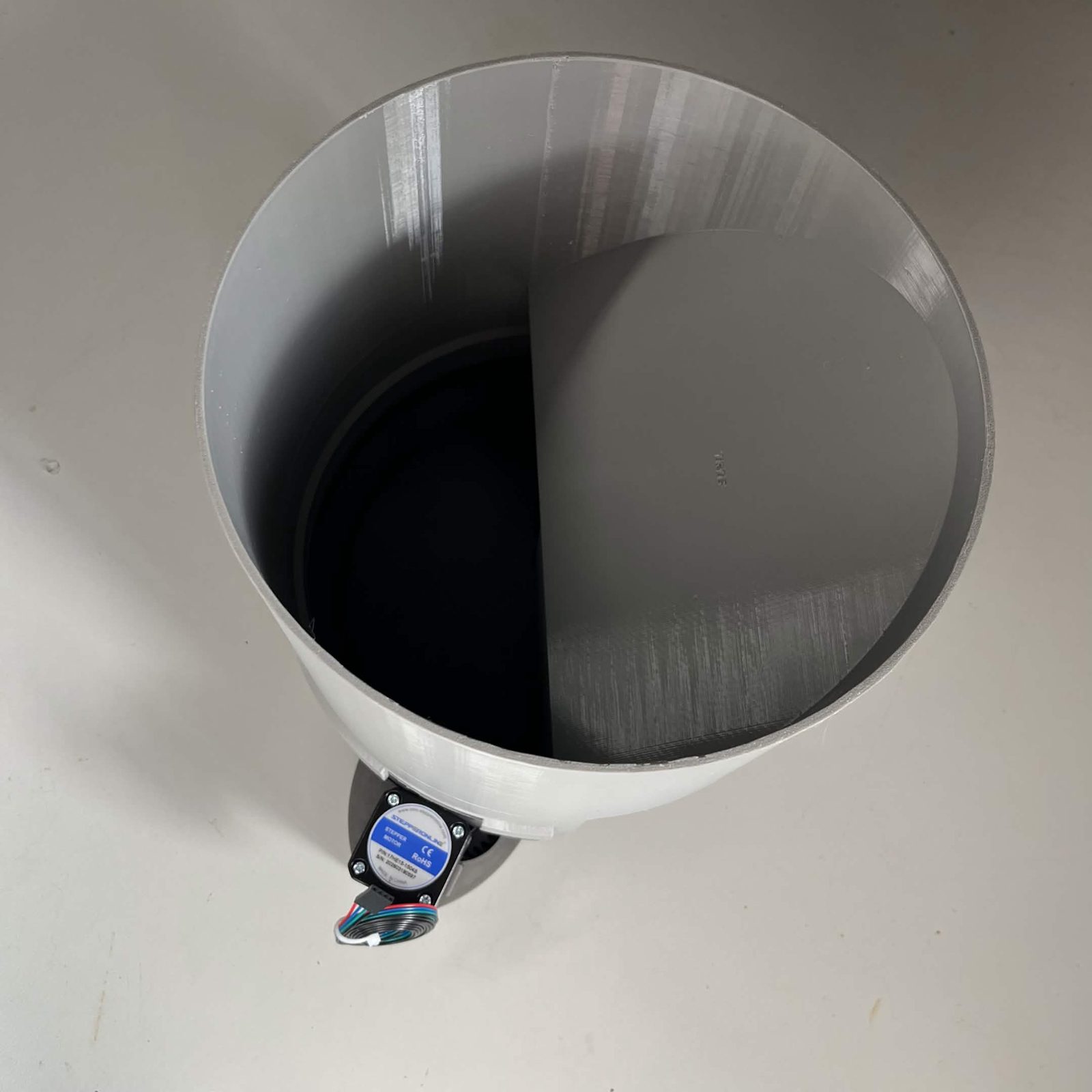Looking down into the fitted bulk cap: the tall cylindrical wall standing on the channel, the rotor face across the bottom of it, and the stepper motor below at the front