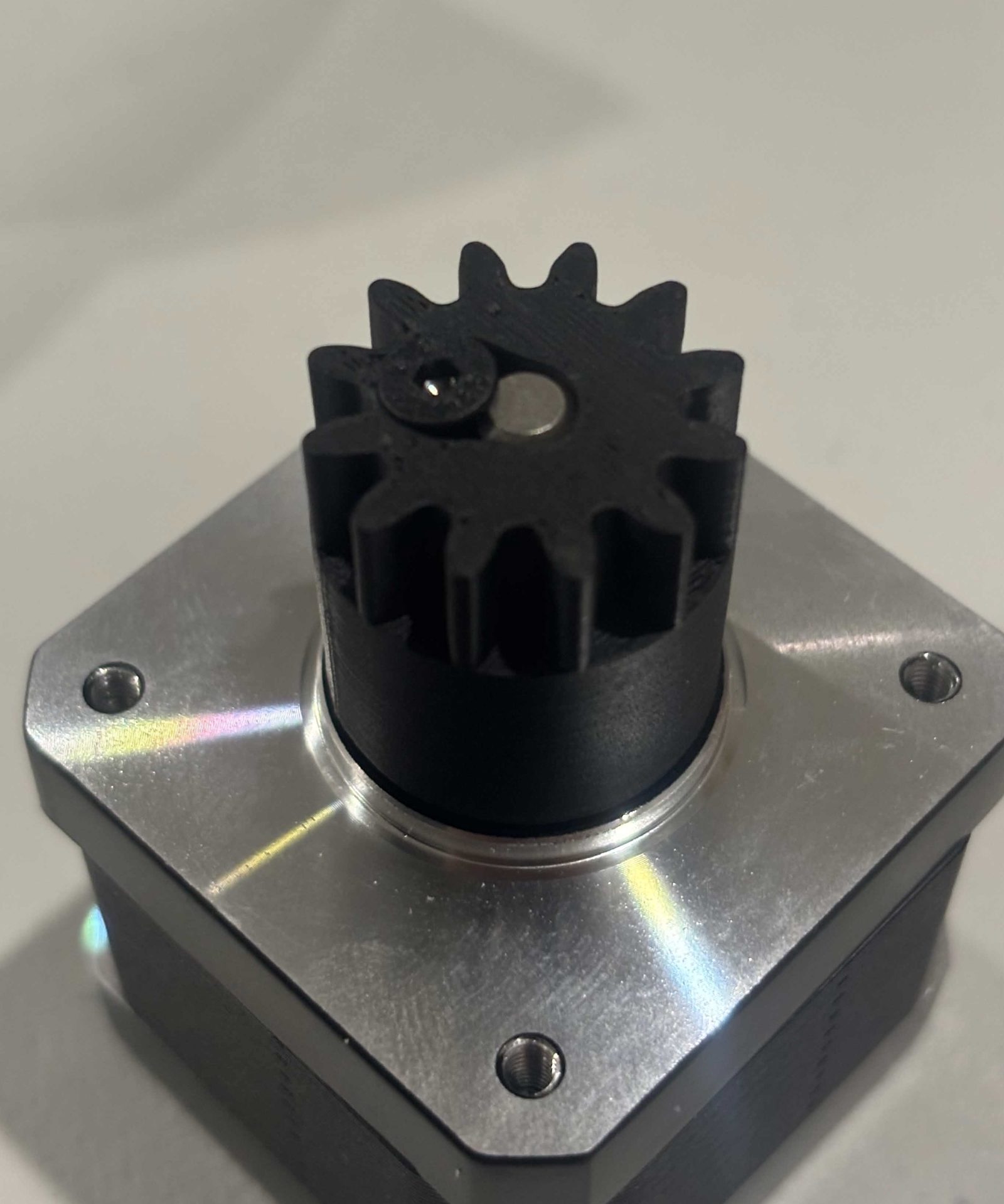 The same gear and motor with the clamping screw driven fully home, its head sitting down in the round counterbore in the toothed end face, and the gear seated against the front face of the motor