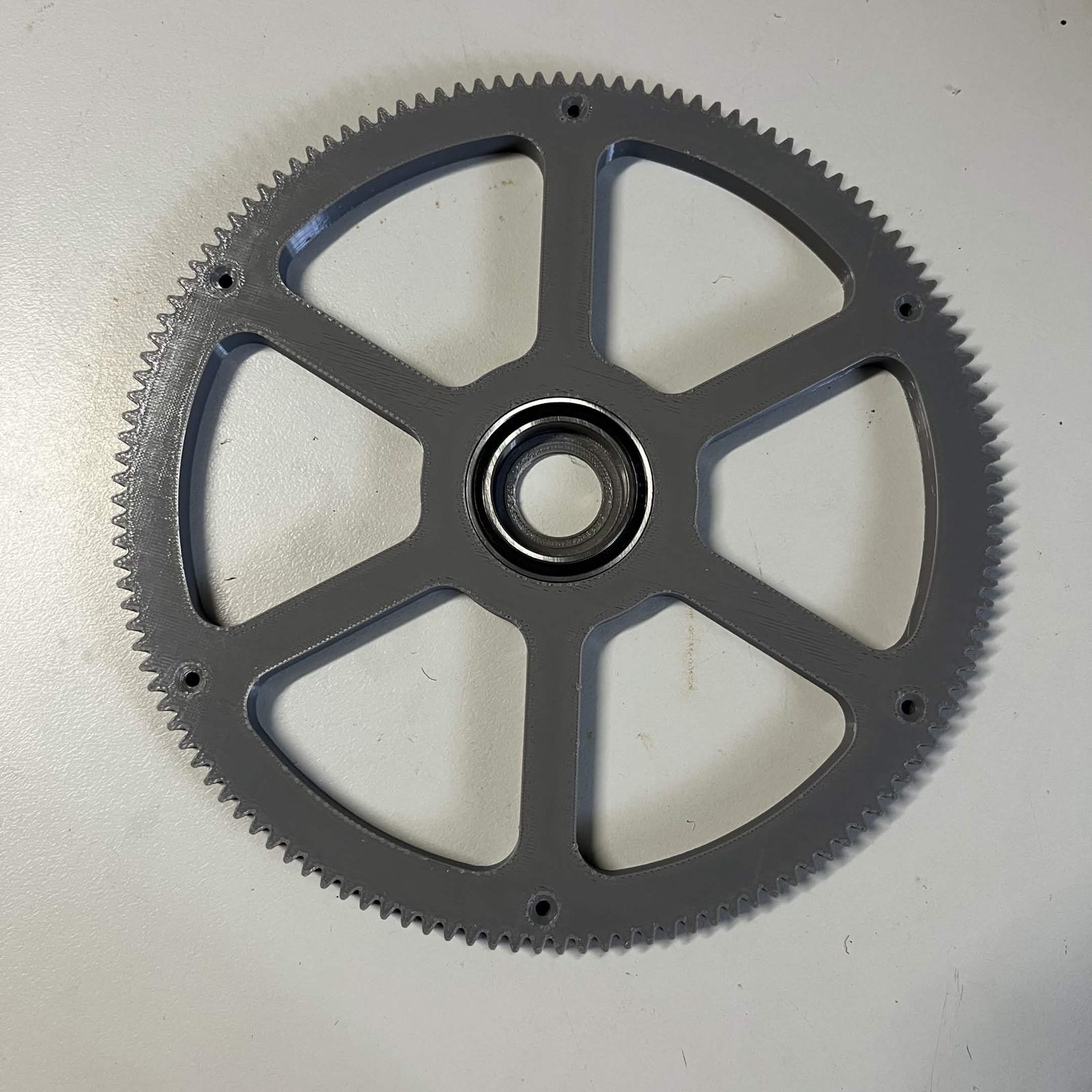 The 130-tooth output gear lying flat with a black-sealed 6806 bearing pressed into its six-spoke hub