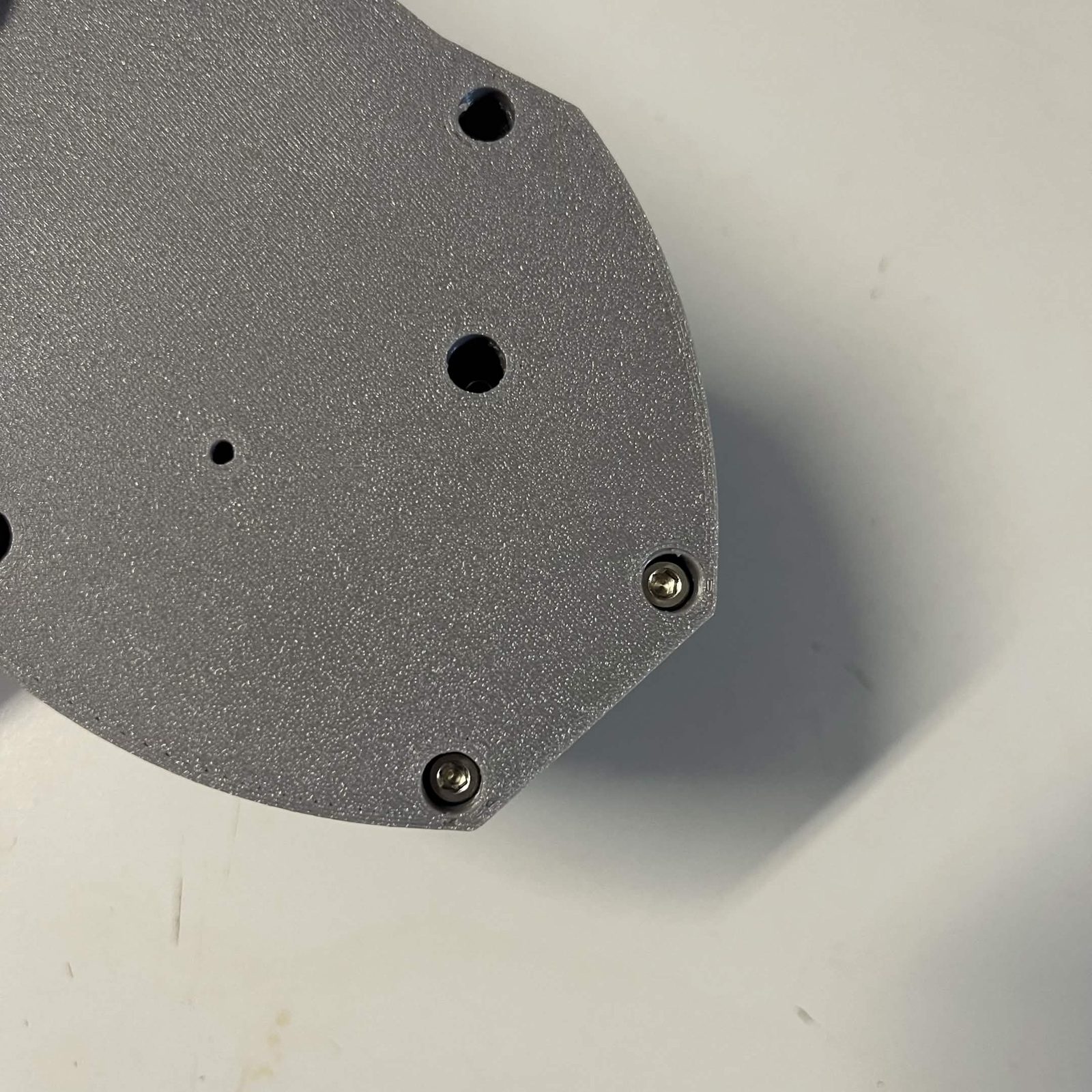 Close view of the grey NEMA bracket, two countersunk screws driven near the edge with further mounting holes beside them
