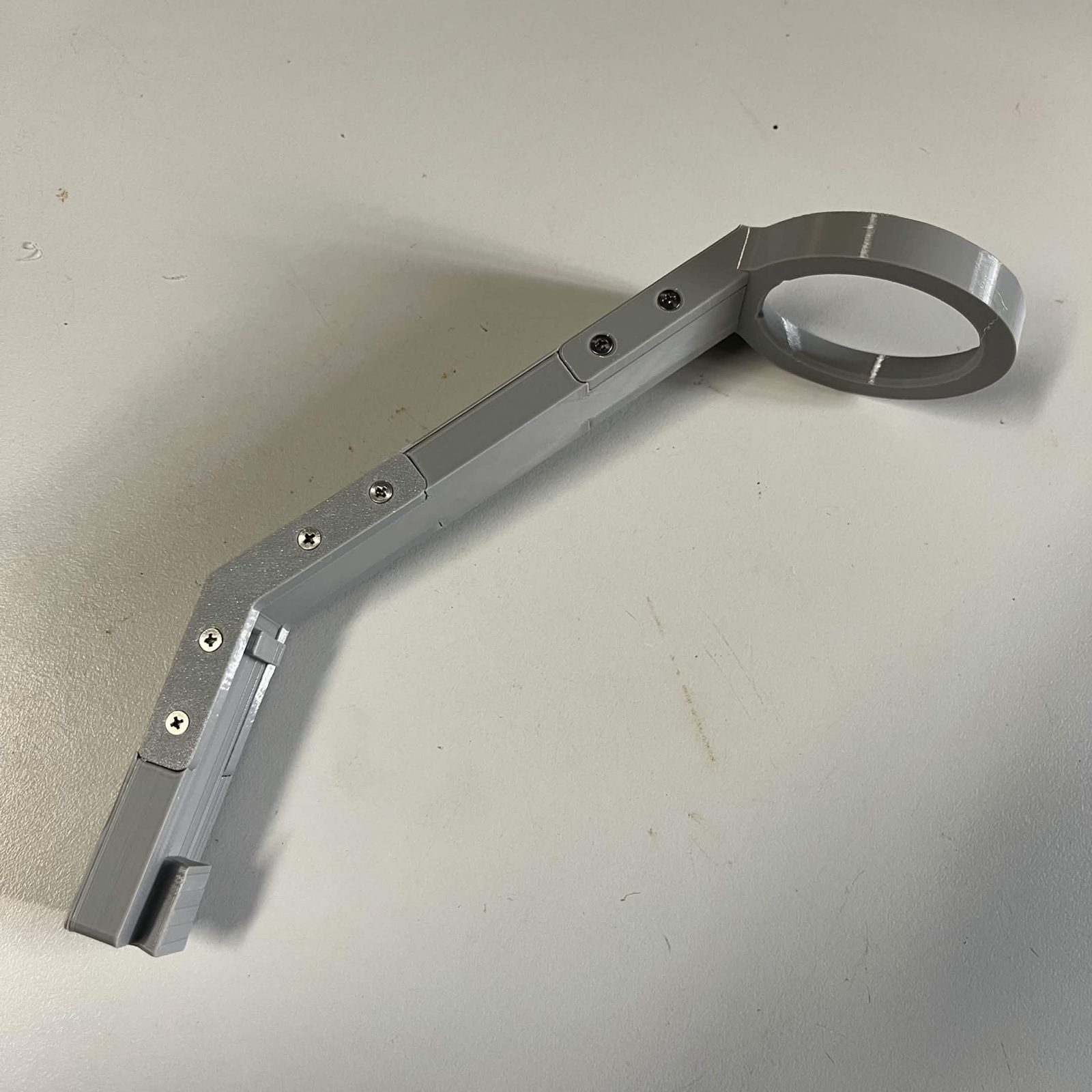 The whole camera lamp arm assembled on the bench: the dovetailed mount end, the bracket running along the joint with its screws, the bend, and the lamp ring at the far end