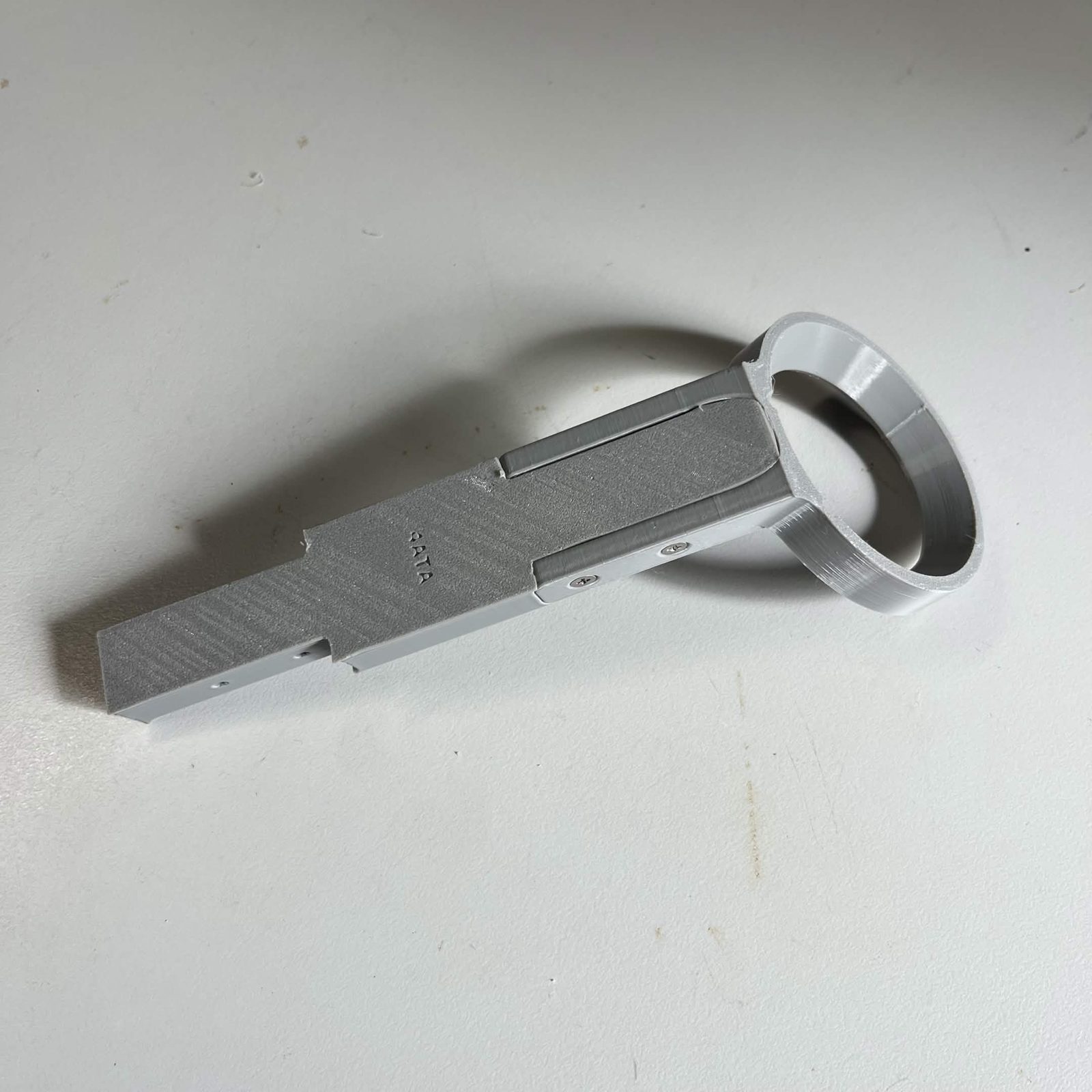 The far section of the camera lamp arm lying on the bench, the lamp ring at one end and the shaped mating end at the other