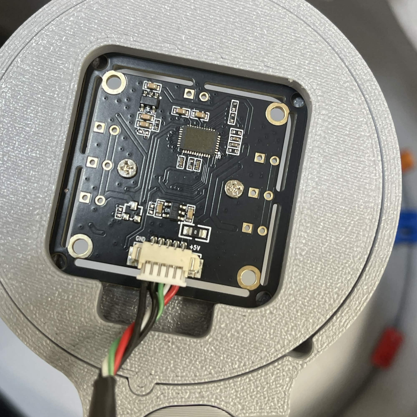 Looking straight down on a finished lamp: the grey cover with its square opening, the 720p camera board seated in the clasp inside it, and the ribbon lead leaving the board's connector through the slot below