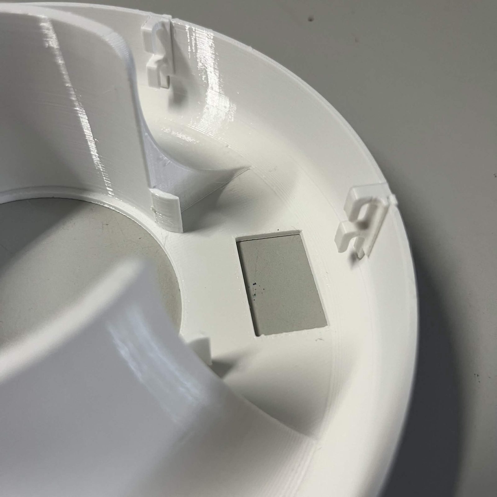 A closer view of the same reflector, two of the hooks standing off the rim and the grey rectangular plate on the flat between them