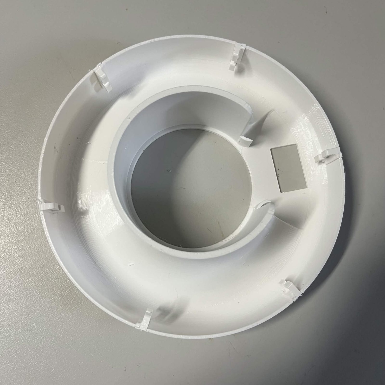 The printed lamp inner reflector lying face up, ivory white, with six LED hooks clipped evenly around its rim and a small grey rectangular plate sitting on the flat