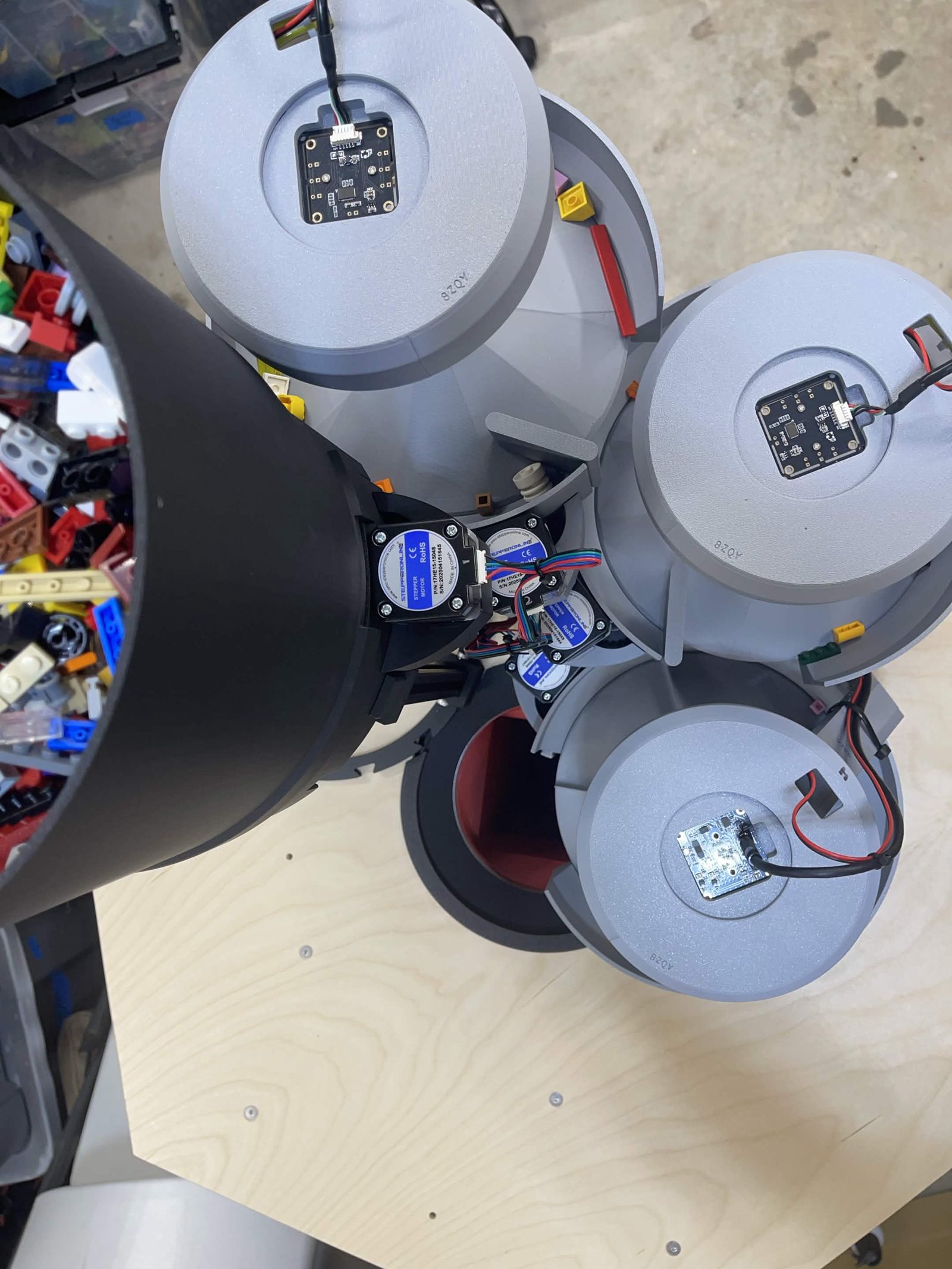 The feeder from above on a built machine: three camera lamps over their channels, each with its camera board in the middle of the cover and its leads running off to one side, with the black bulk hopper at the left and the steppers grouped in the centre