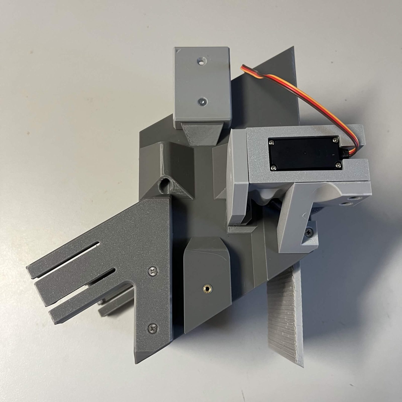 A built chute core standing on the bench: the printed core with the door module and its bearing covers on one side, the MG995 servo in its bracket above, and the funnel brackets projecting from the left