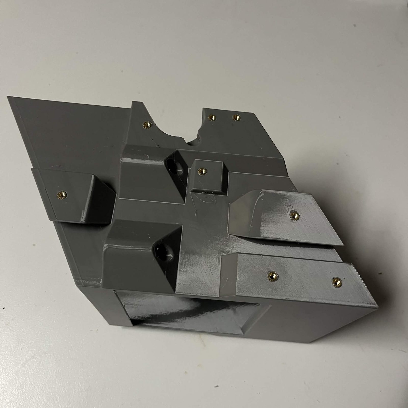 One long side of a printed chute core, brass heat inserts pressed into all eight pockets on that face
