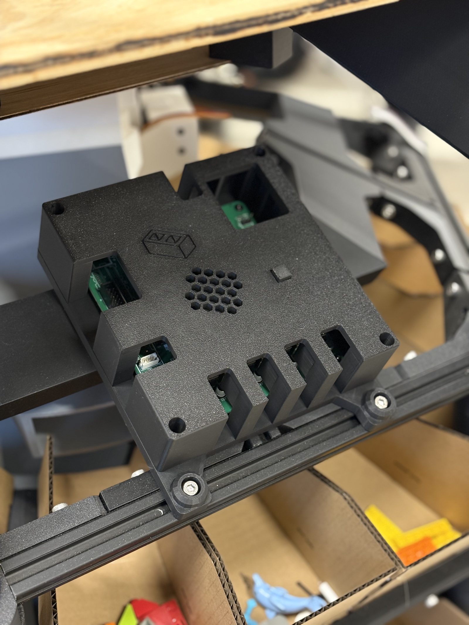 The finished control board housing bolted down onto a 2020 aluminium extrusion under the machine's frame, with two socket head screws through its clamp bosses
