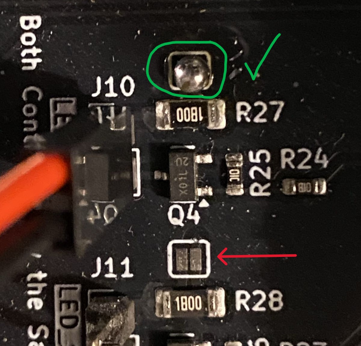 Annotated close-up of the control board between ports J10 and J11: the solder jumper above R27 is circled in green with a green tick beside it and carries a blob of solder across both pads, and a red arrow points at the jumper above R28, which is two bare pads with a gap between them