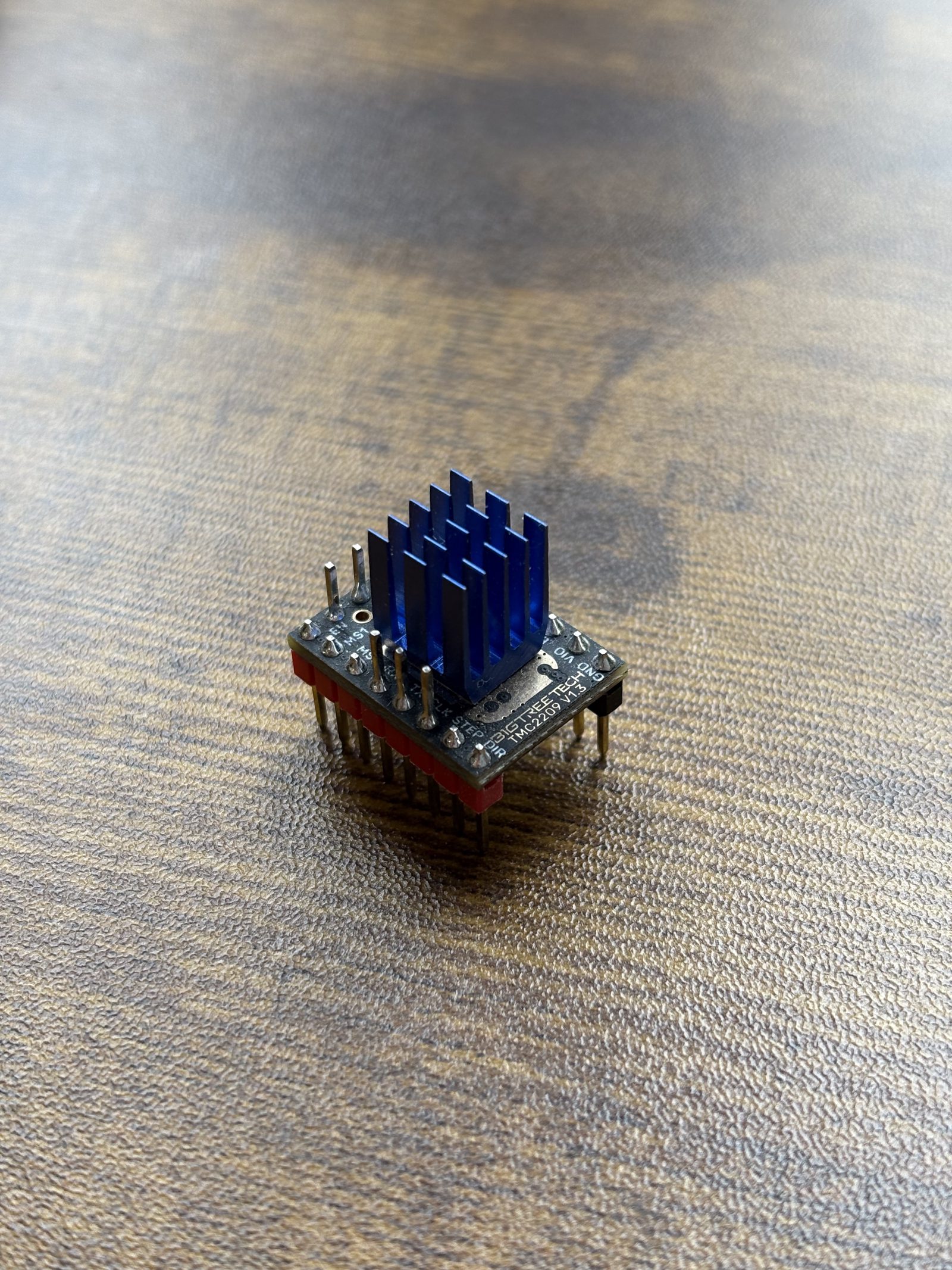 A single TMC2209 V1.3 driver module standing on a bench, blue heatsink upwards, with its pin names readable around the edge