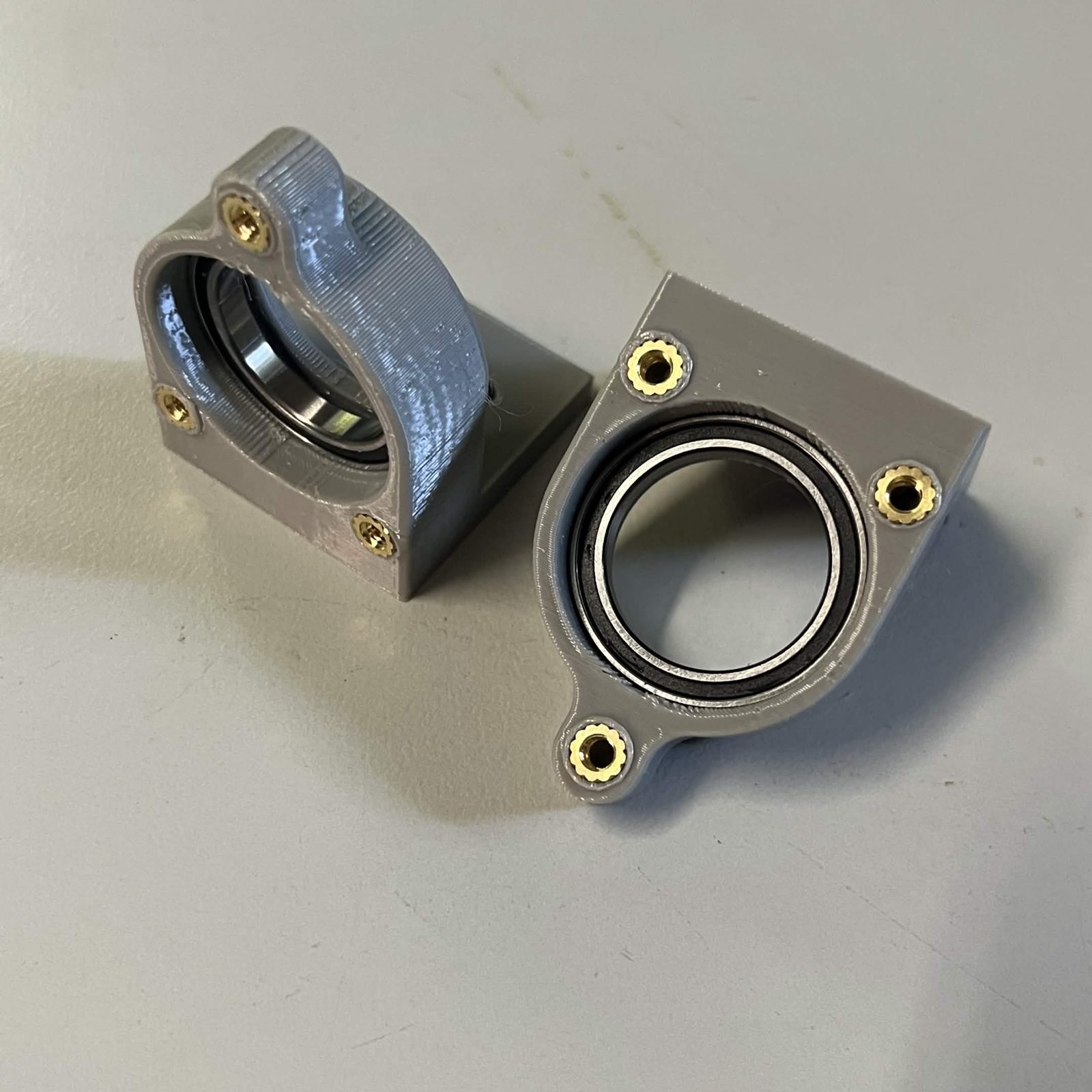 Both printed bearing holders with a 6704-2RS bearing pushed into each bore, a ring of printed plastic still visible around the bearing's outer race, and three brass heat inserts around each face