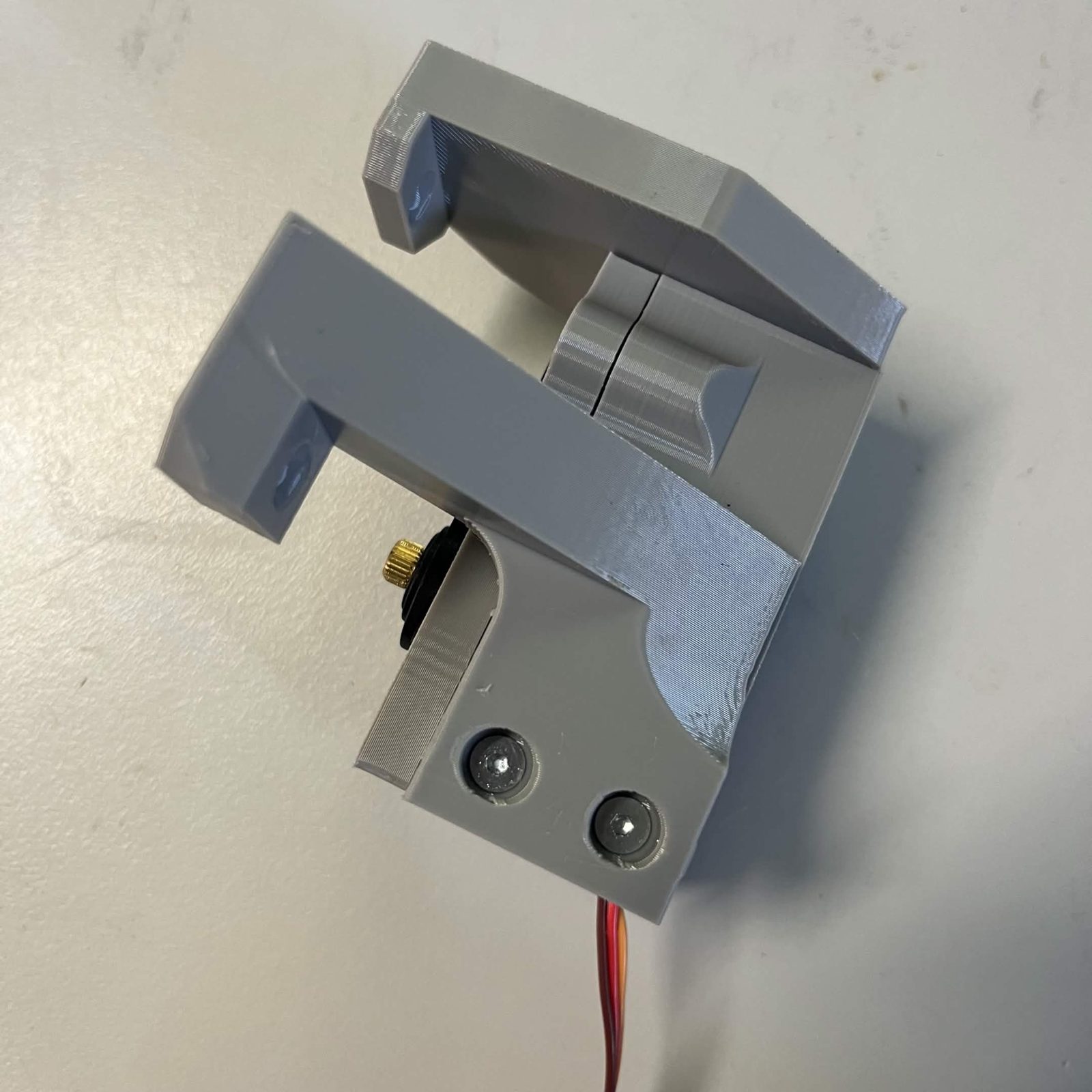The finished bracket from below with both arms fitted, the lower arm's two screw heads sunk at the bottom of their round counterbores and the servo's output shaft visible between the arms