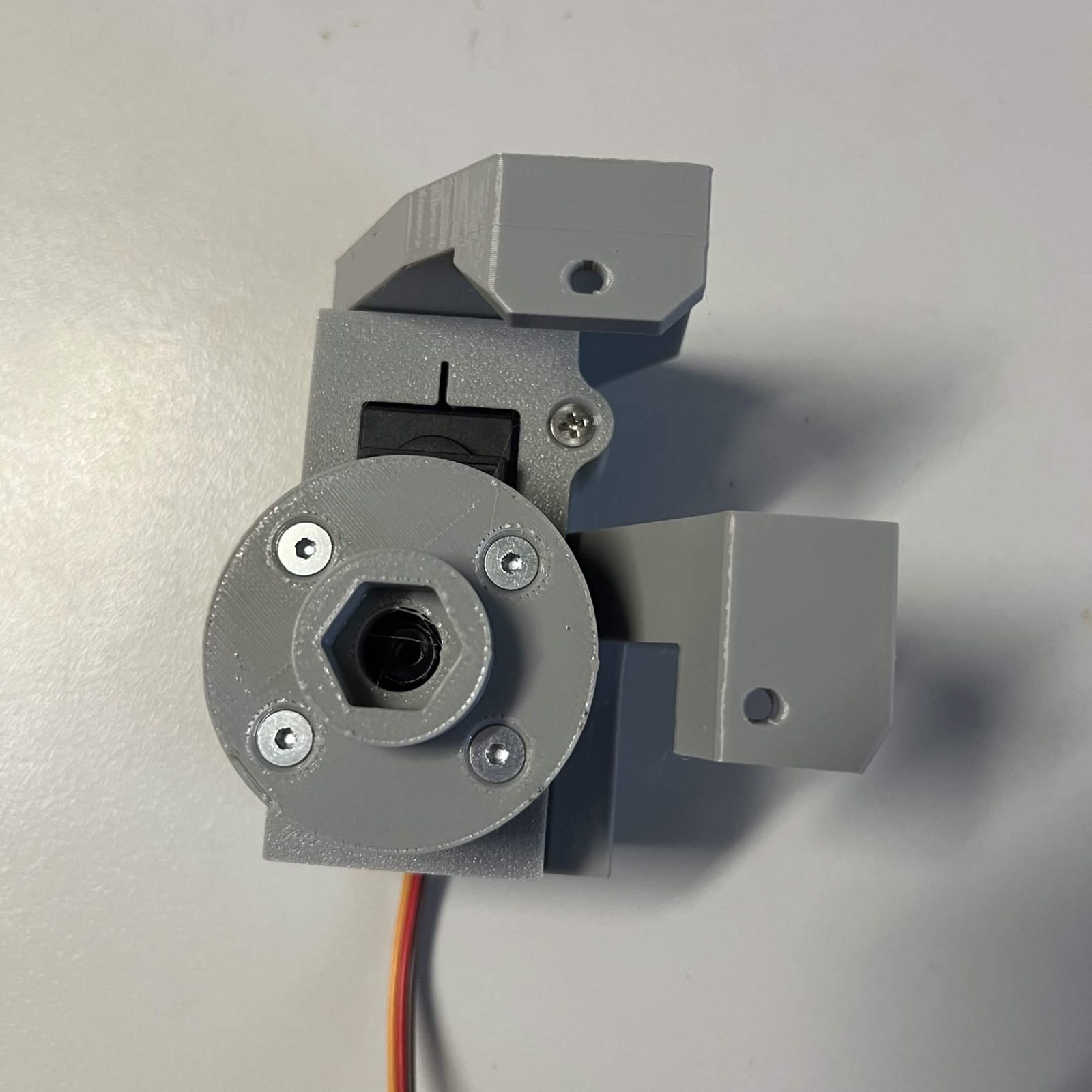 The servo bracket bolted to the chute core with the servo adapter fitted on the servo's output, seen face on, the adapter's four screws and hex socket visible