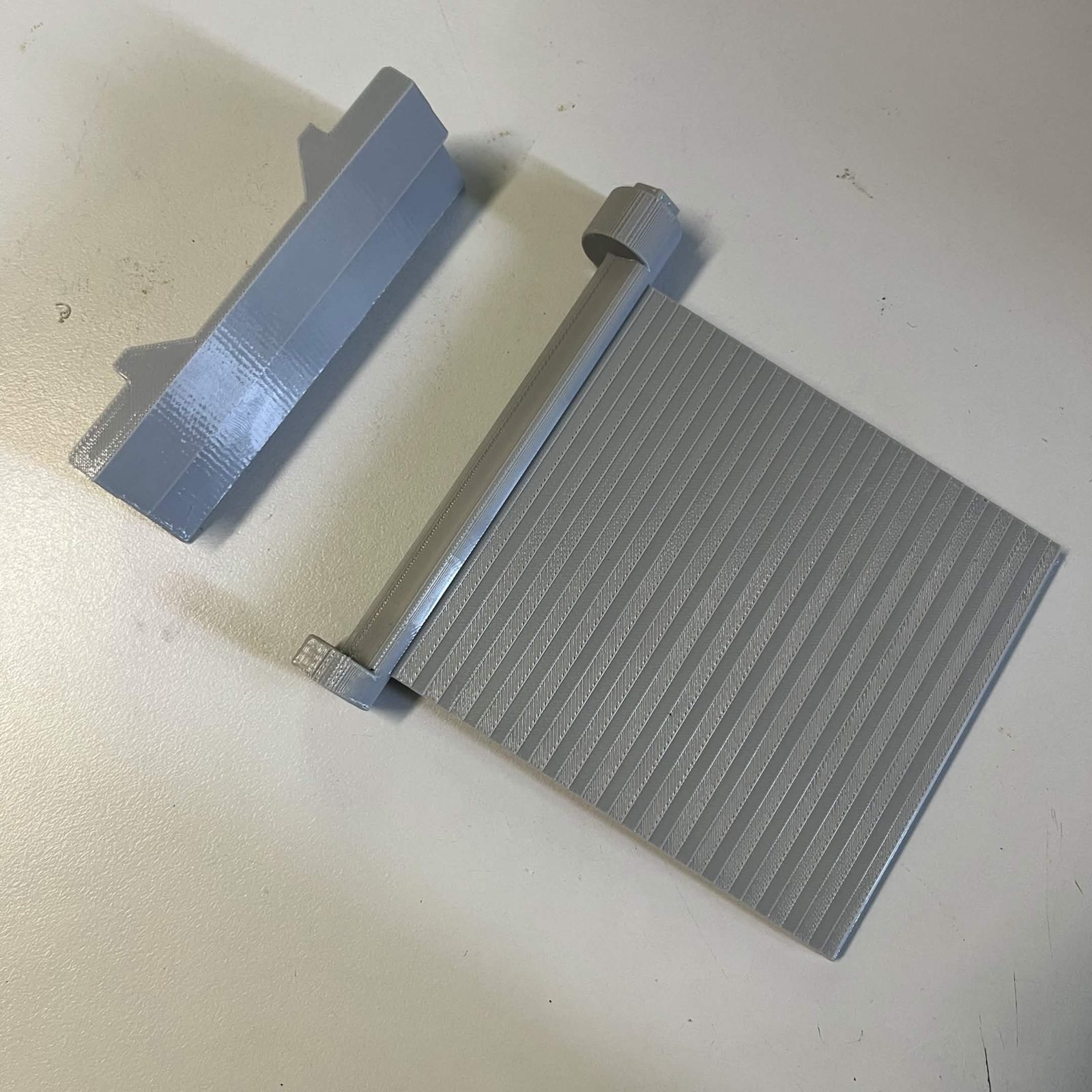 The printed chute door lying beside the bearing race before assembly, the door's shaft running along its top edge with the hexagonal spigot at one end, and the race's stepped profile facing the shaft