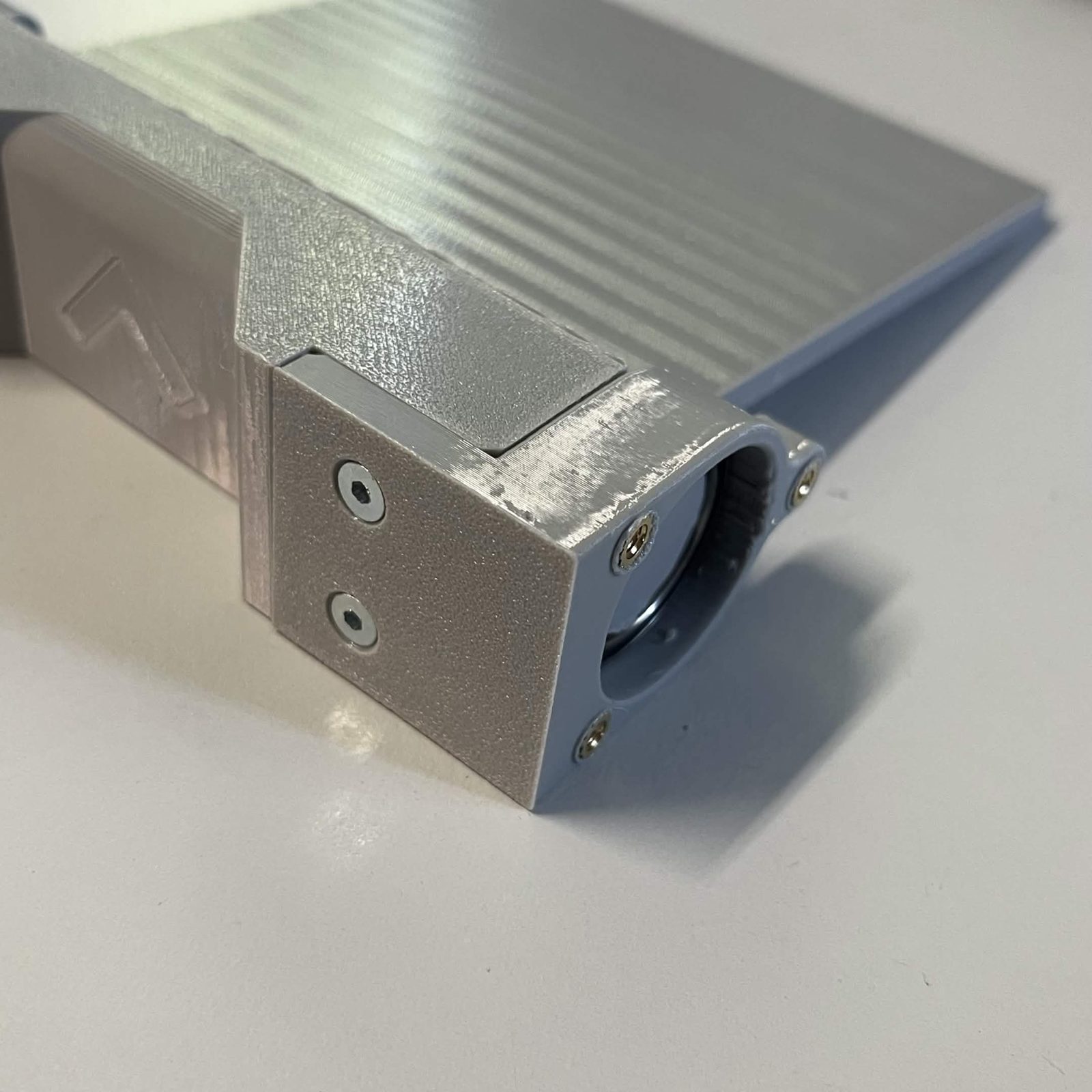 Close view of one end of the assembled flap: the bearing holder bolted to the end of the bearing race with two countersunk screws in its face, the bearing seated in its bore with the door's shaft through it, and the door plate above