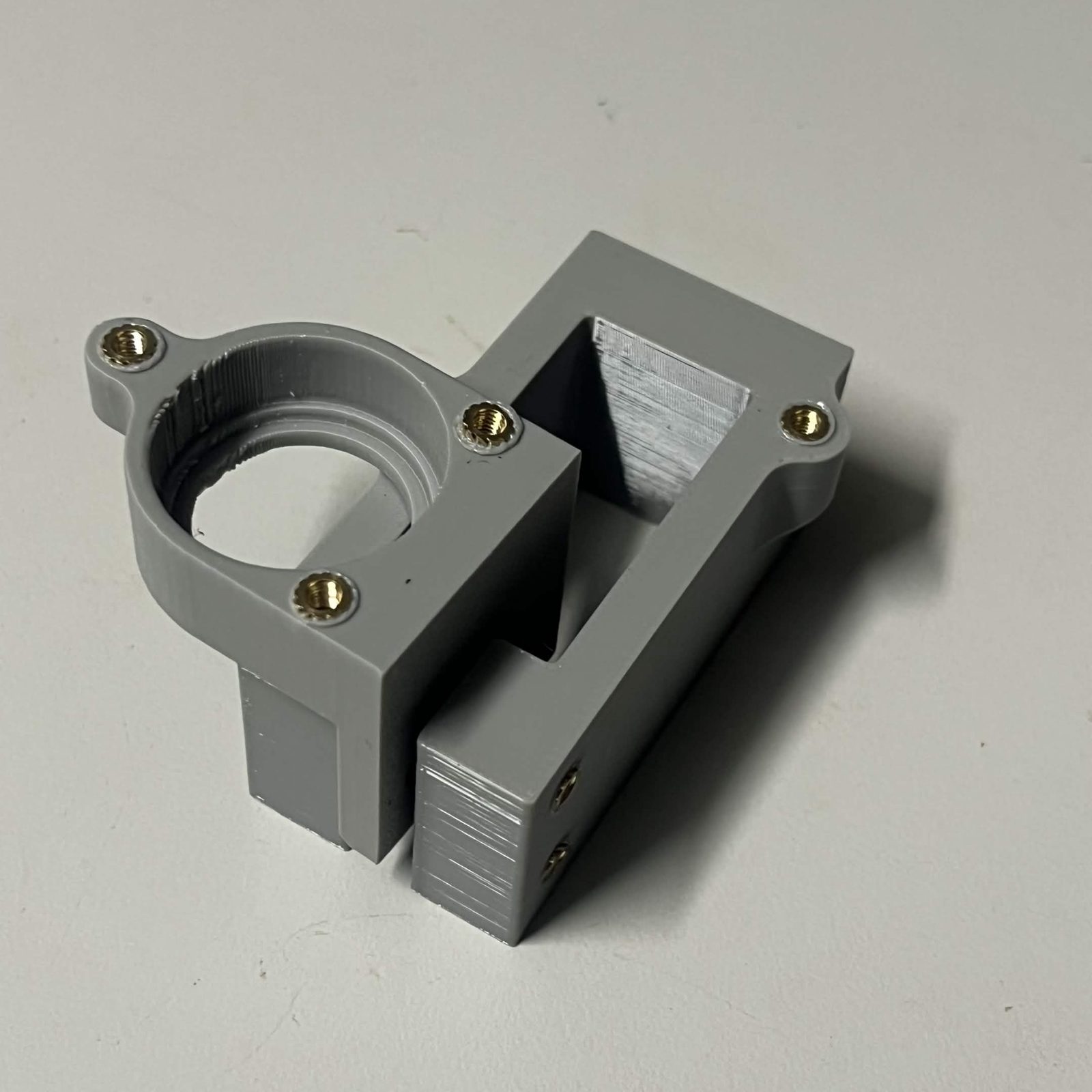 A bearing holder with its three brass inserts standing against the open servo bracket housing, which props it upright on the bench