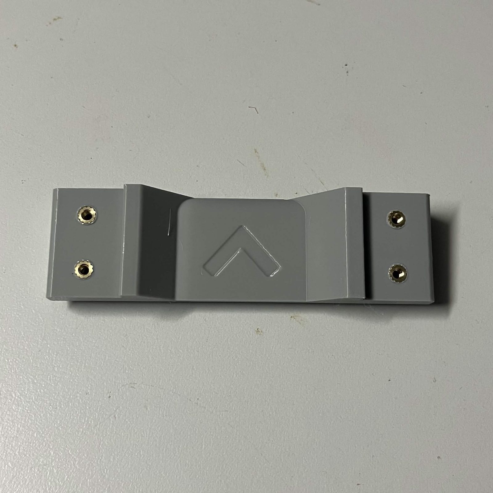 A printed bearing race lying flat, brass heat inserts in the two pockets at each end and a raised chevron in the middle of the same face