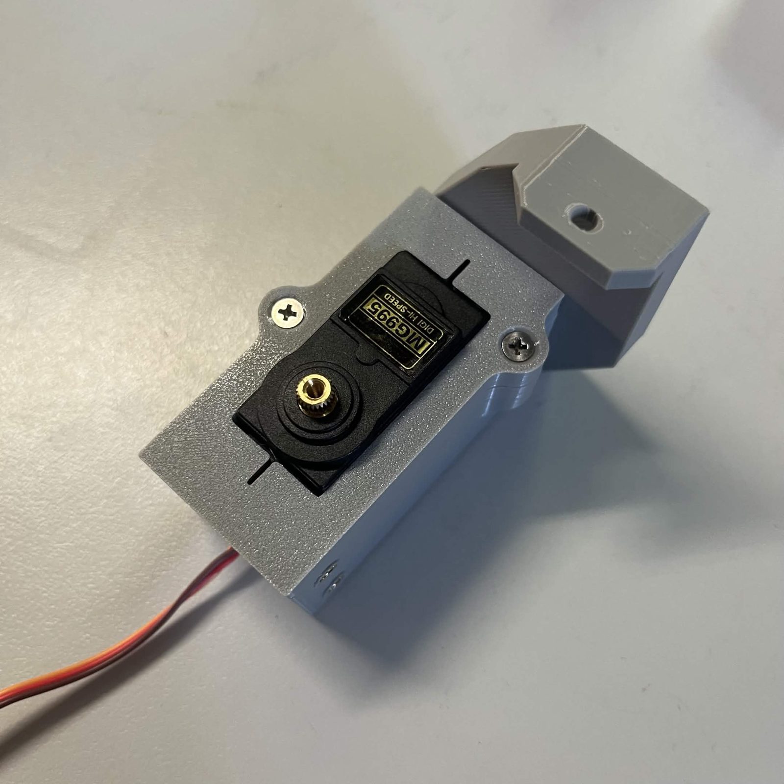 The servo bracket housing with the side arm bolted to it, seen from the cover side, the slab standing proud of the housing with a single empty hole in its foot