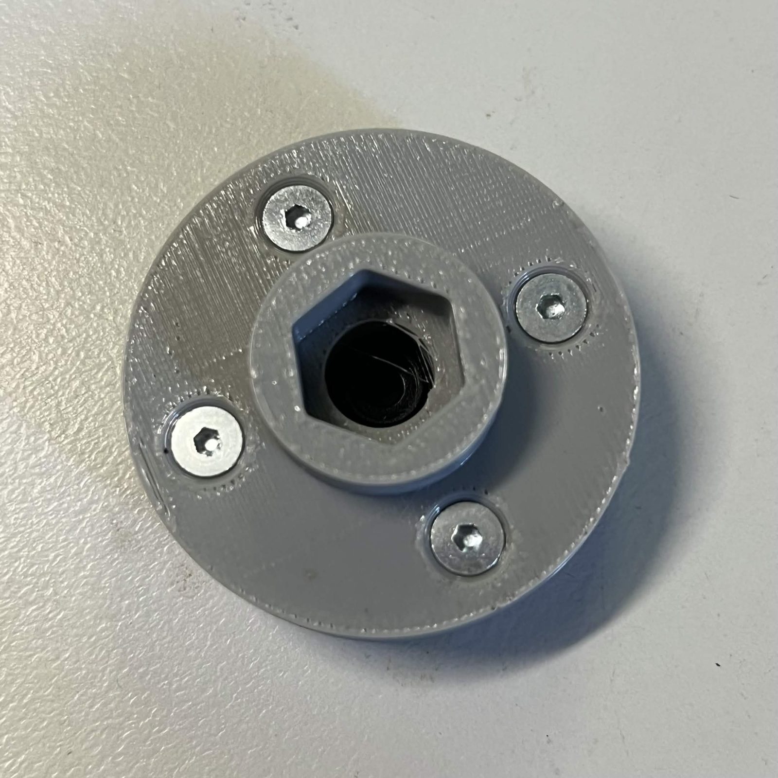 The same adapter from the flap side: a raised hub with a hexagonal socket in the middle and the four countersunk screws driven from this face around it