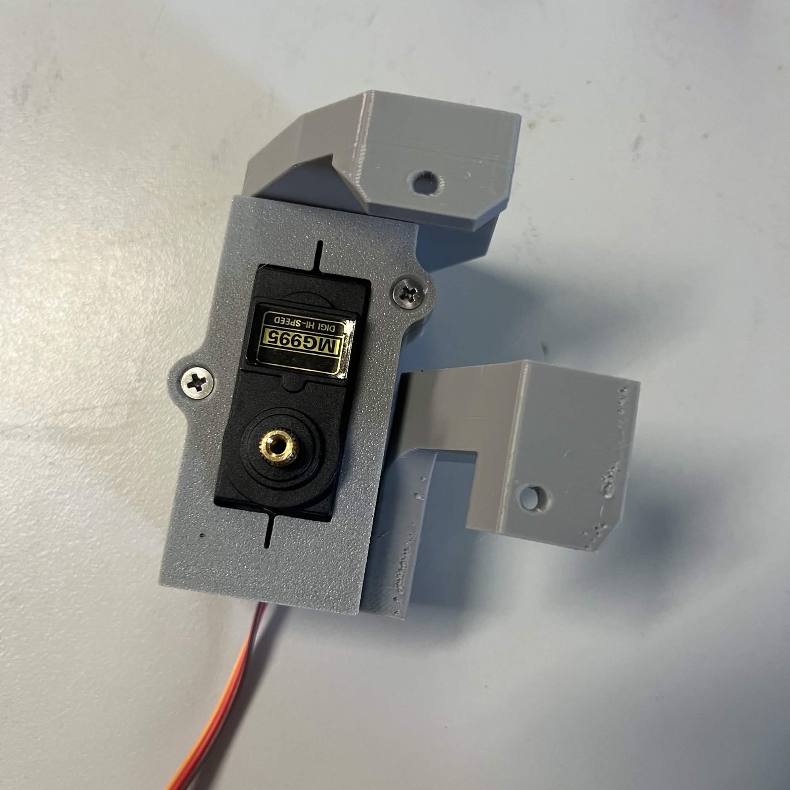 Both arms now on the housing: the side arm slab across the top and the lower arm projecting from the right-hand face with an empty hole in its raised end