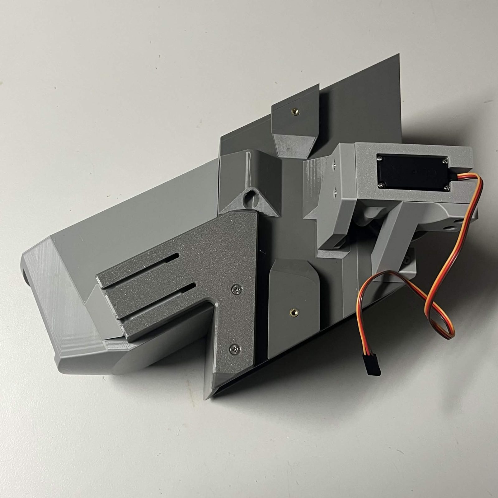 A funnel hung on its two brackets on a chute core lying on the bench, the wide funnel mouth to the left with a bracket arm across each side rail, and the servo in its printed bracket at the far end of the core
