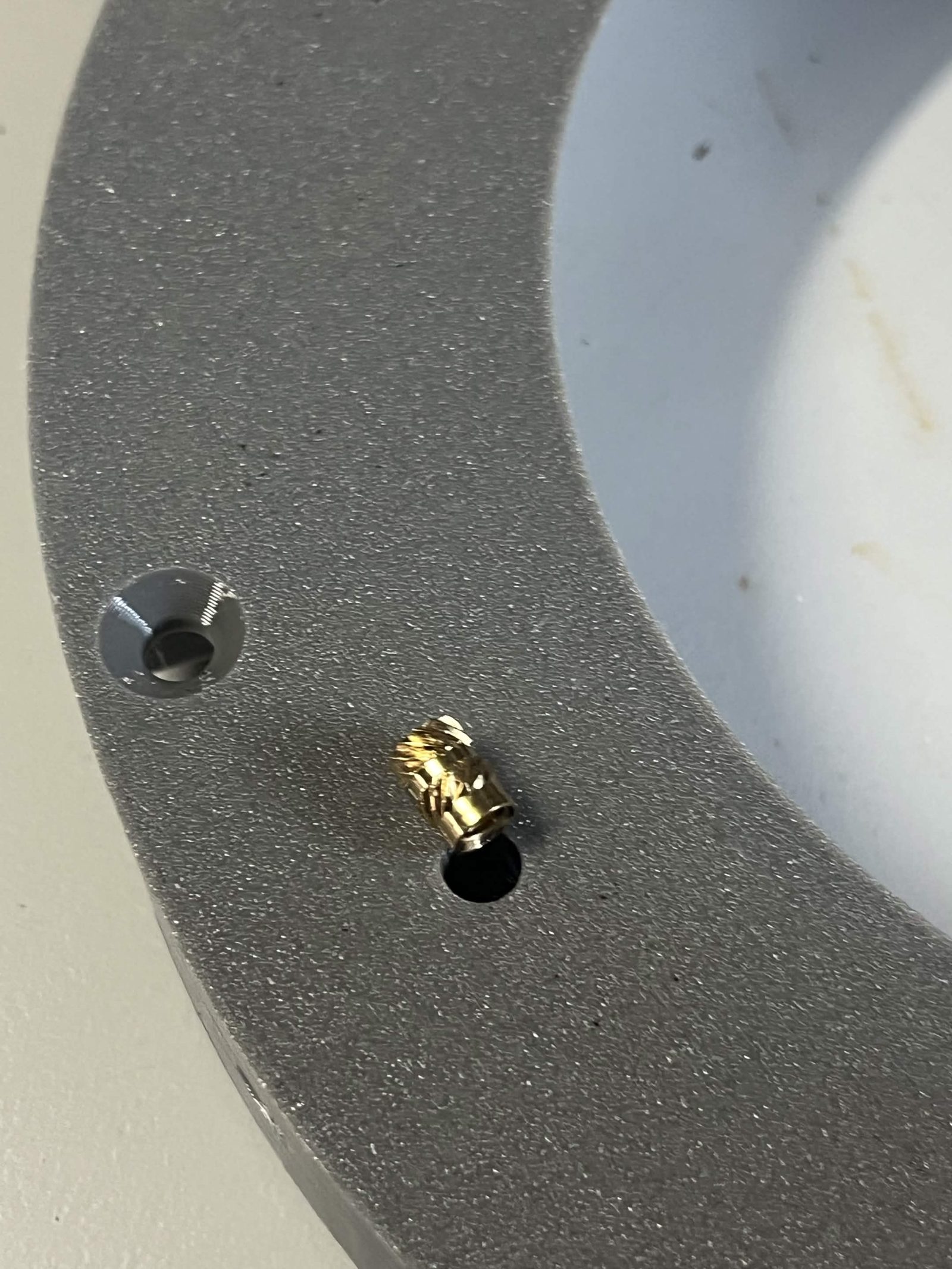 Brass heat insert standing over its hole in a printed part, thinner end down, next to an insert already installed flush