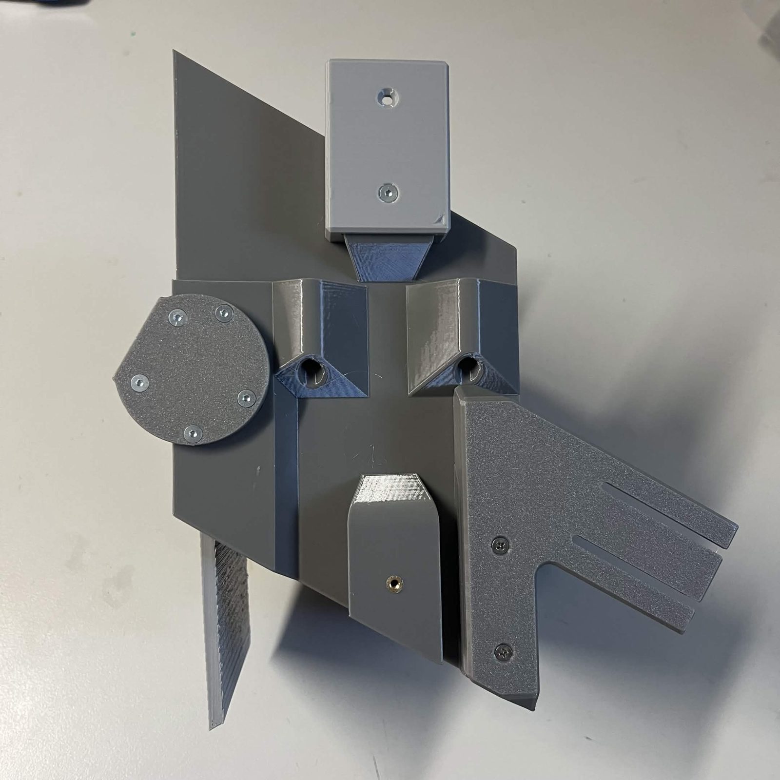 A light grey layer connector standing proud of the top edge of a chute core, screwed to the core through the lower of its two countersunk holes with the upper hole empty, other sub-assemblies on the core around it