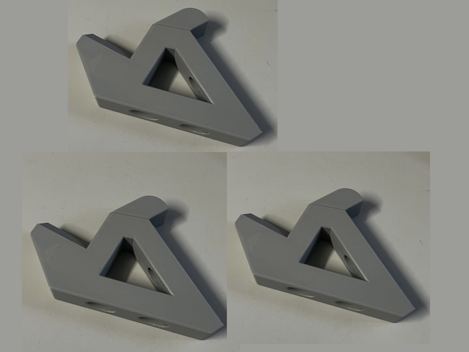 Three views of the same printed part on a white background: the Lazy Susan extrusion mount with its hold in place bolted under it, a grey wedge with a triangular window through its web and counterbored slots along its bottom face