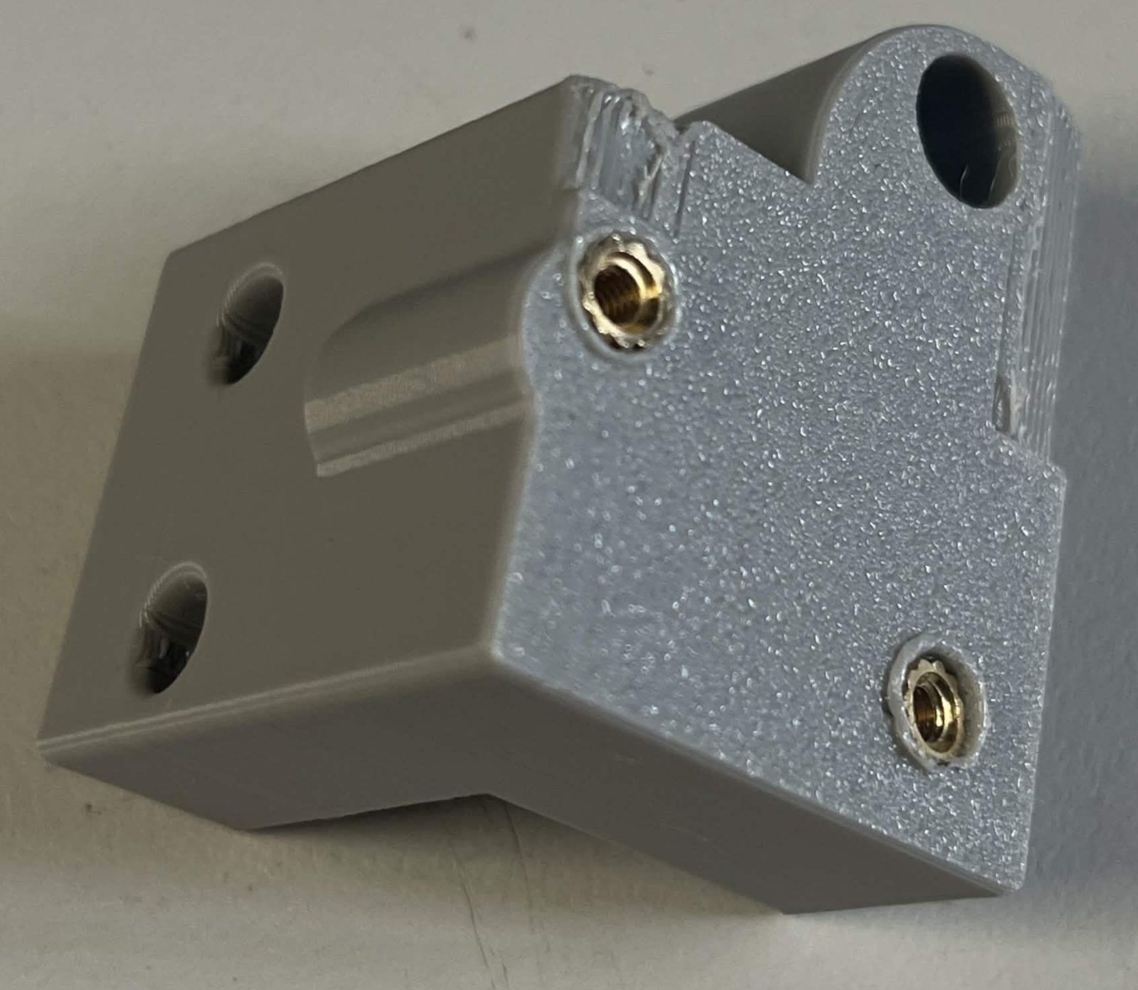 The grey Limit switch housing, showing two brass M3 heat inserts on the angled face where the roller lever limit switch mounts, with the dowel pin hole above them