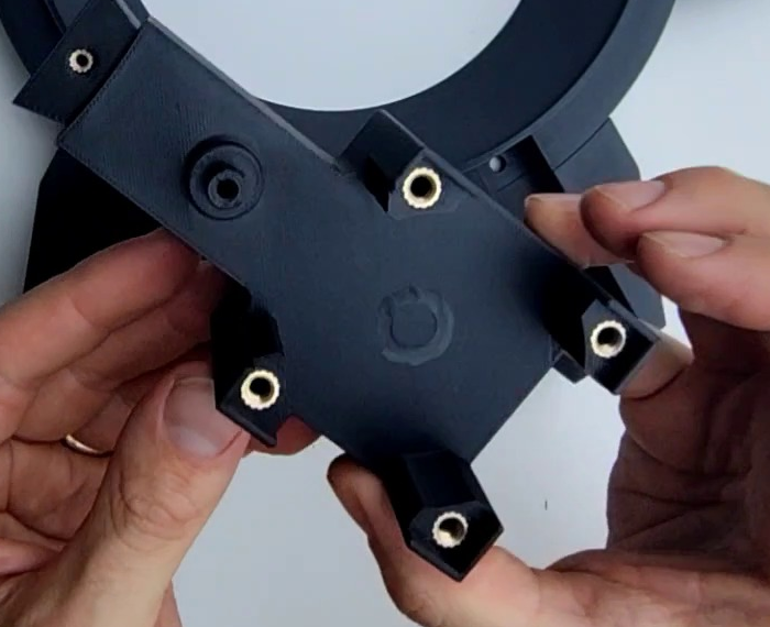 The Interface NEMA 23 bracket held up, showing four brass M5 inserts on the top edges and one M3 insert on the long tail