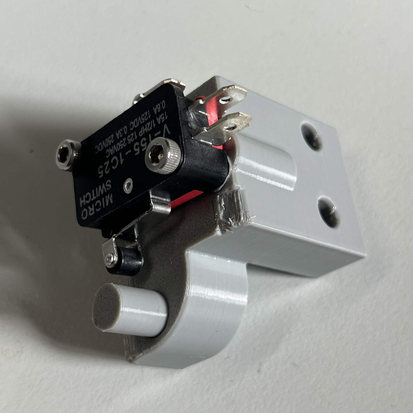 The same limit switch housing from behind, showing both M3 screws through the switch body and the dowel pin standing proud of the housing