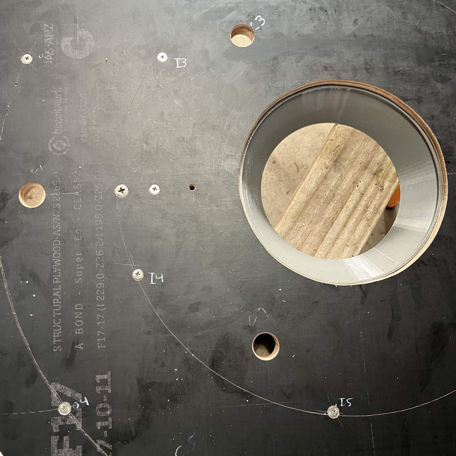 The assembly flipped onto its Top plate, the plate's face up with the marked I and O holes around the centre opening