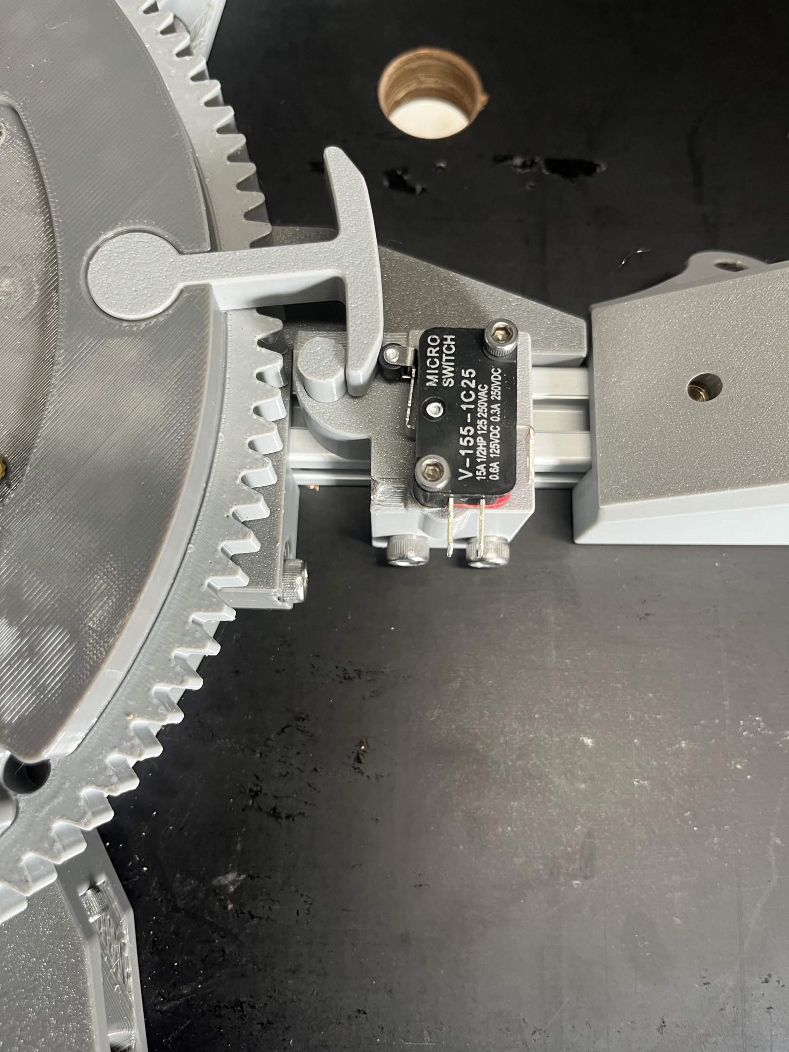 Close view of the Limit switch hammer swung in between the roller lever limit switch and the printed dowel pin, beside the chute's ring gear teeth