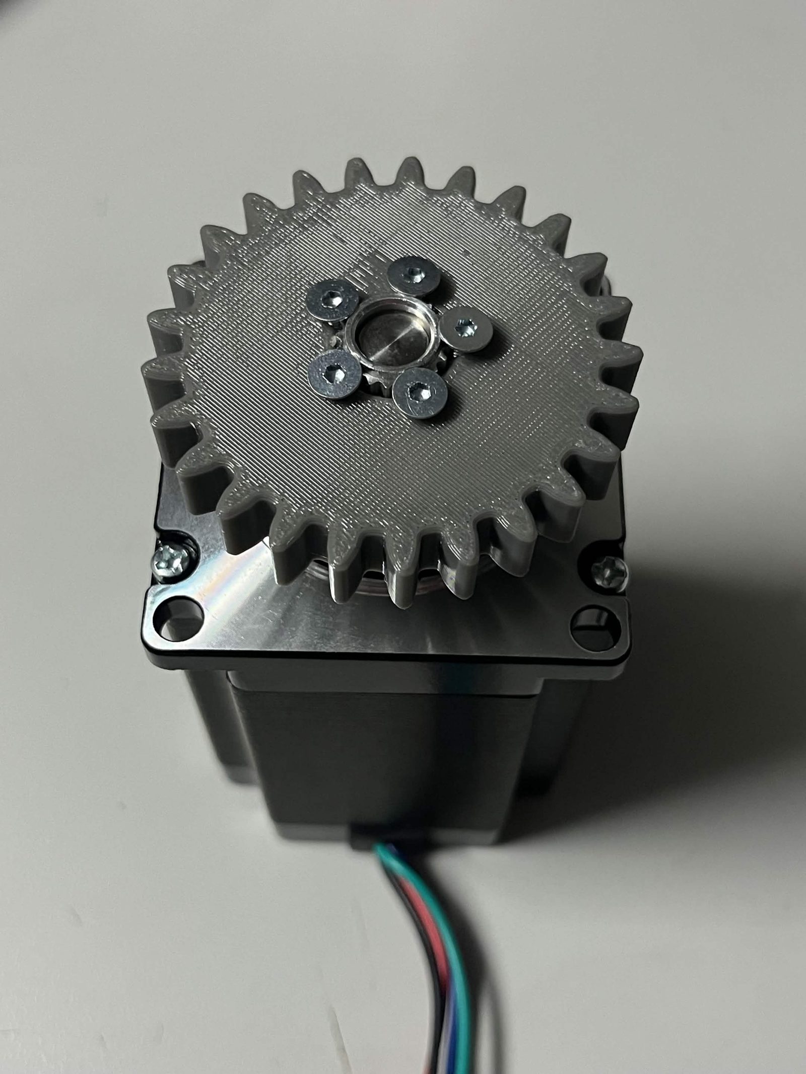 Grey Interface spur gear secured over the timing pulley with five countersunk screws
