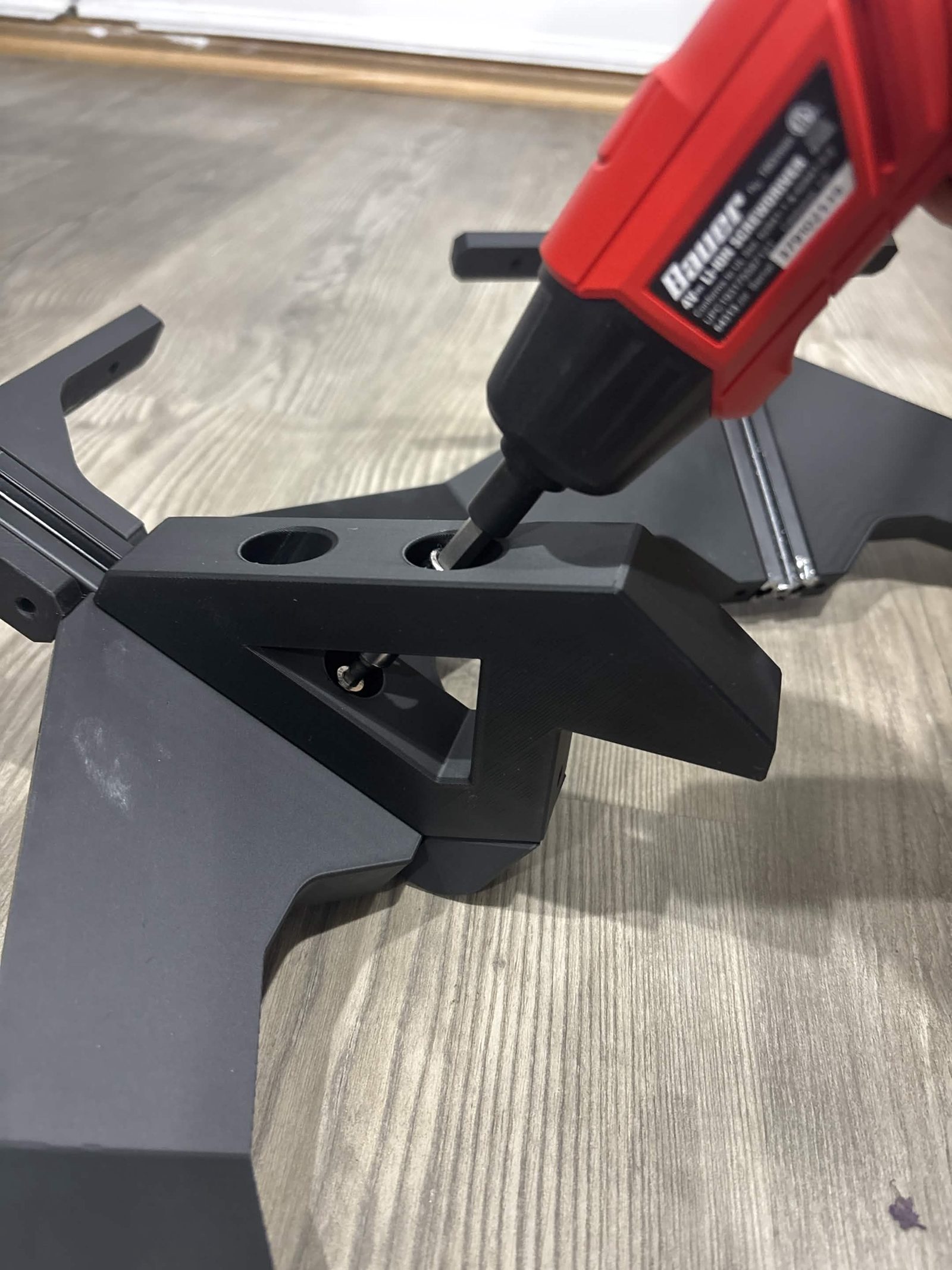 An electric screwdriver driving one of the two screws in the top face of the extrusion mount while it sits on the frame