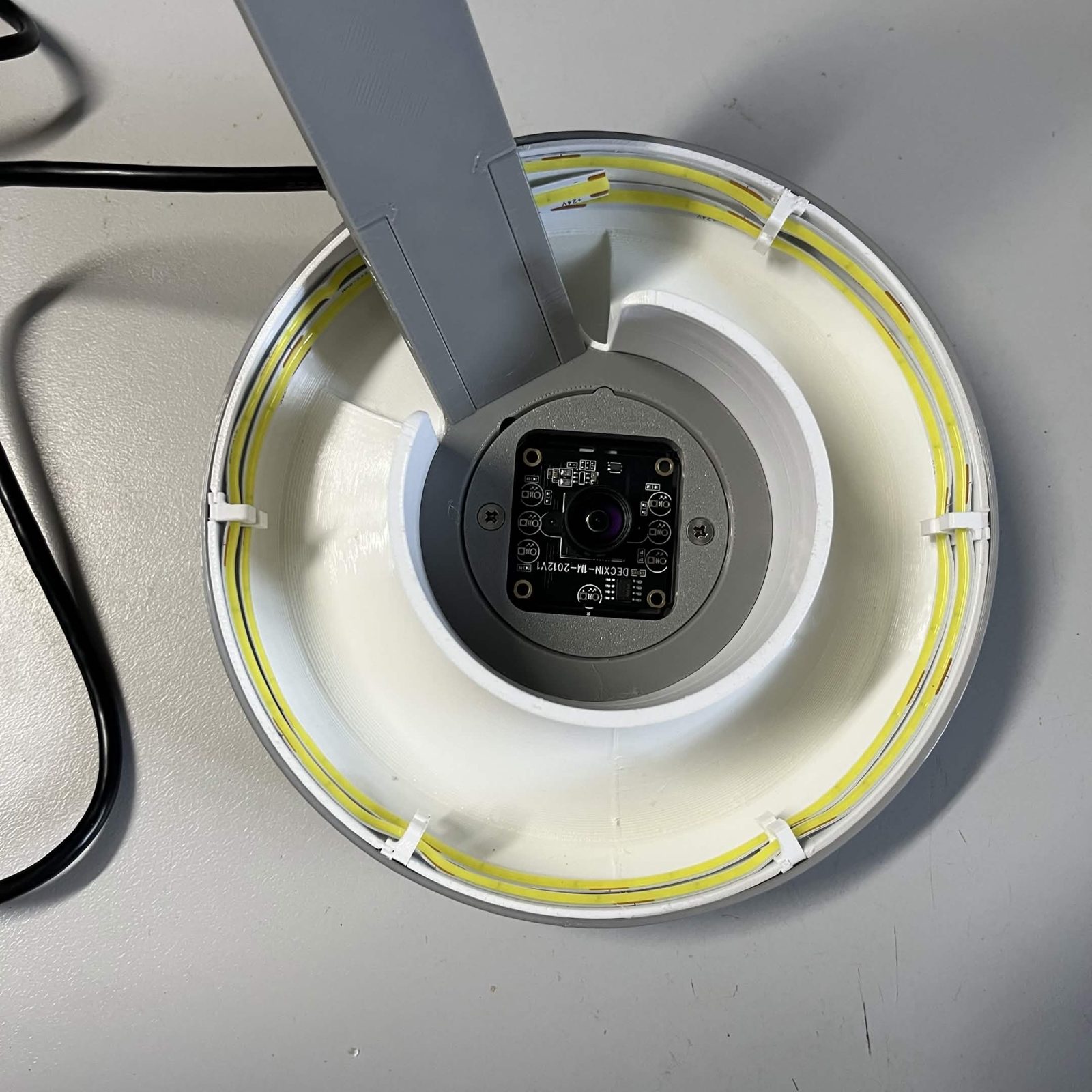 Looking up into the reflector from below: two turns of LED strip round the skirt held by the hooks, the arm coming down through the middle, and the clasped camera seated in the ring at the centre with its lens facing out