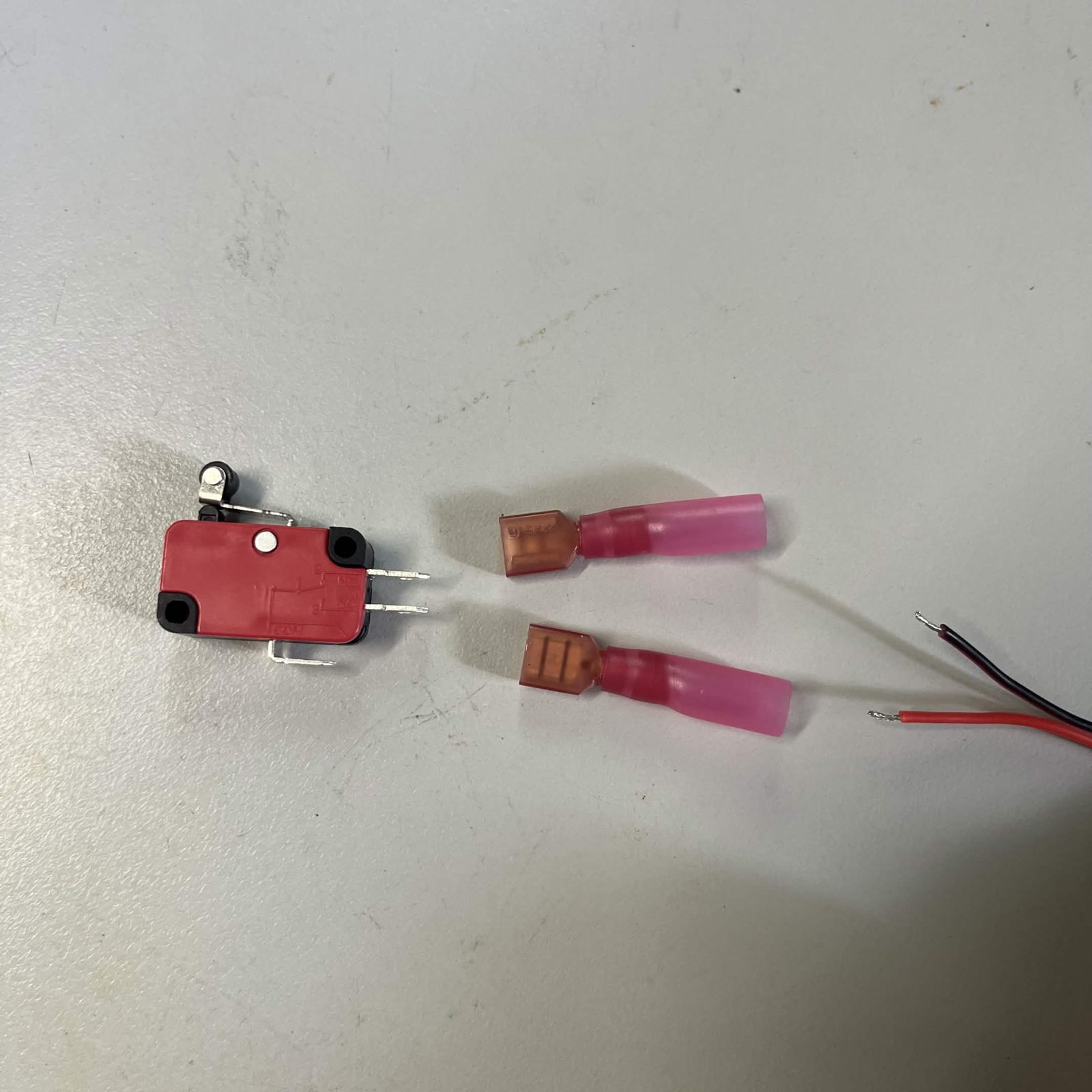Laid out on a bench: the red roller-lever switch with its three bare tabs, two insulated quick-connect receptacles already crimped onto short leads, and the stripped end of a red and black 22 AWG (0.33 mm²) pair