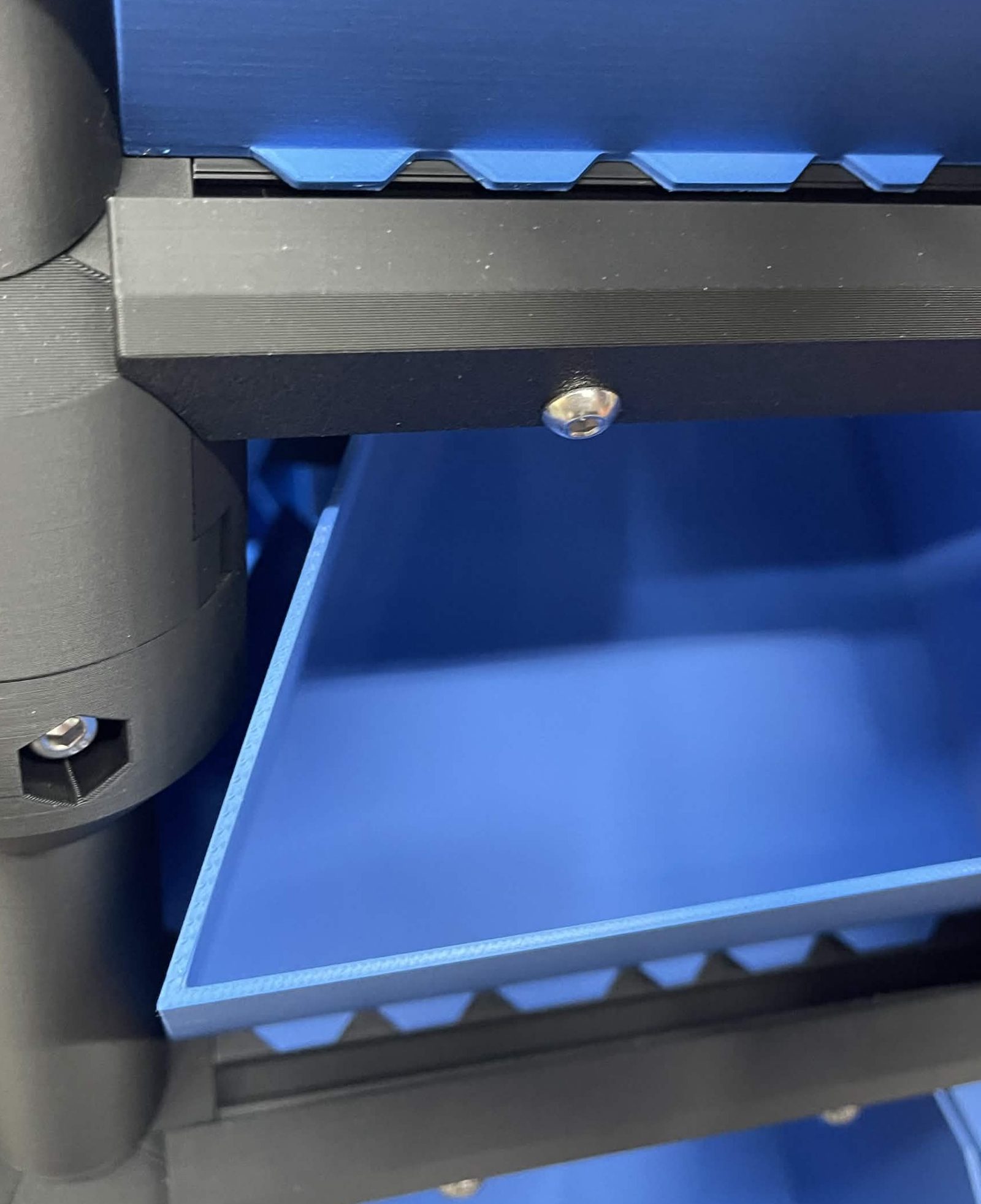 Close-up of two bin retainer rails: the upper bin is seated with its castellated front edge meshed into the rail, the lower bin is lifted clear so the rail's own teeth are visible