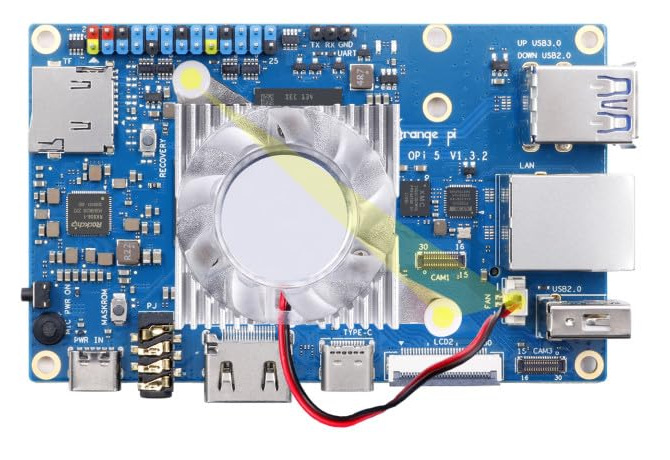 An Orange Pi 5 v1.3.2 seen from above with the heatsink fan already fitted over the SoC in the middle of the board, a white spring pin clipped through the board at opposite corners of the finned block, and the red and black lead running from the fan to a small white 2-pin socket silkscreened FAN