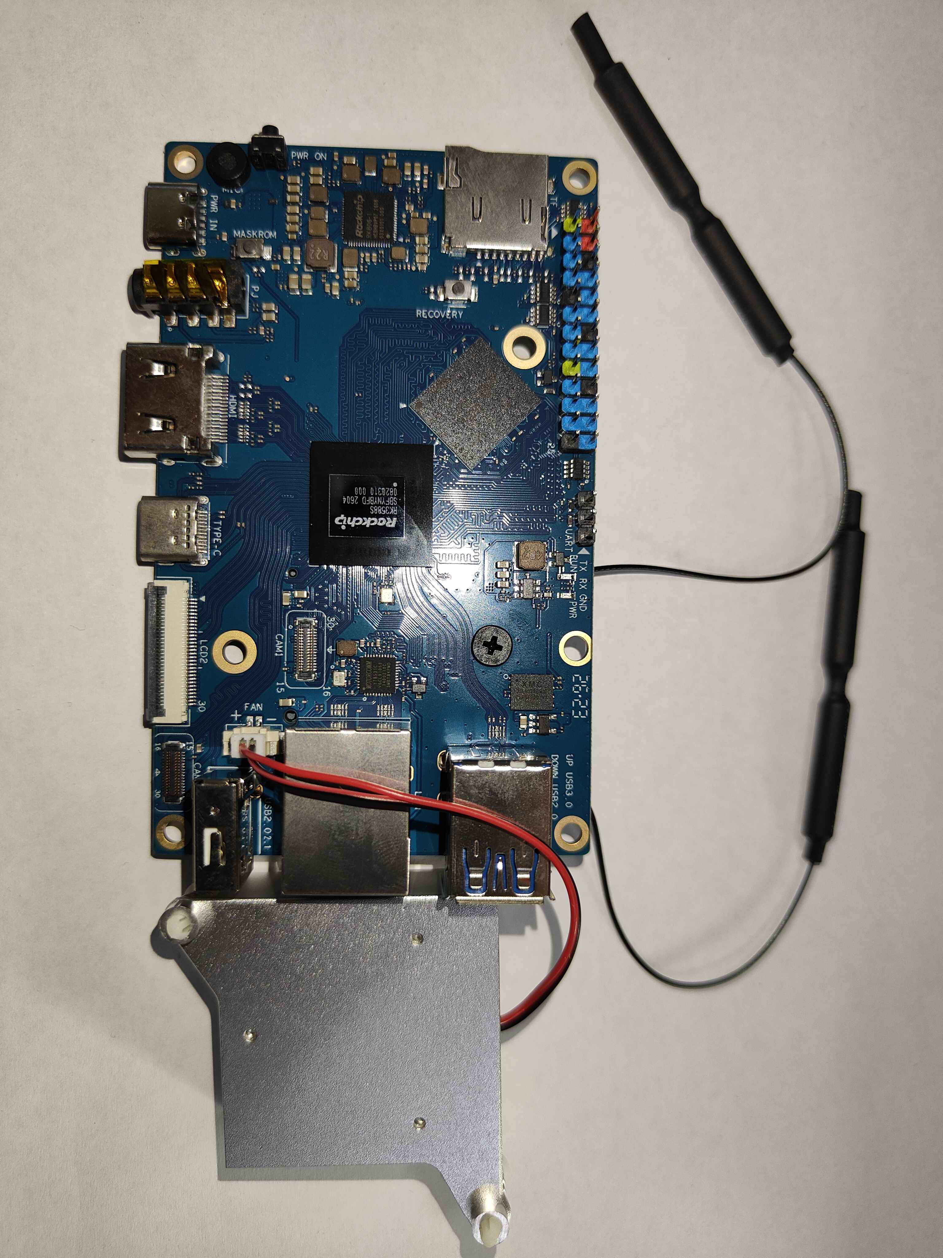 An Orange Pi 5 seen from its top face, with the heatsink fan not yet fitted and lying below the board, and the head of a screw with a cross slot sitting in the board beside the SoC, which is the screw holding the WiFi module on the other face