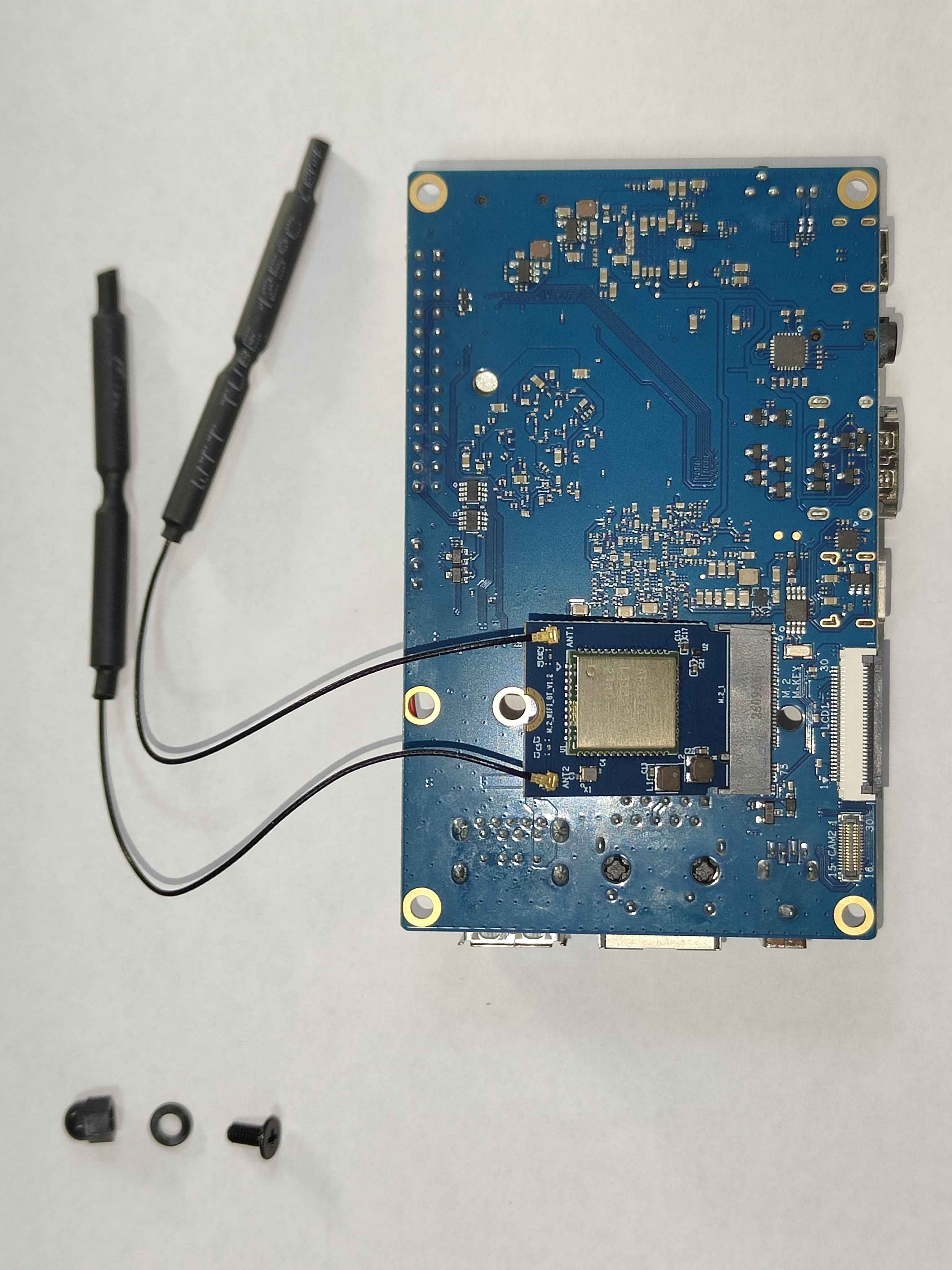 The underside of an Orange Pi 5 with the AP6275P module seated in the M.2 slot and its two antenna leads clipped on, a round hole through the module's free end, and below the board three loose parts in a row: a black dome nut, a black plastic washer and a short black screw