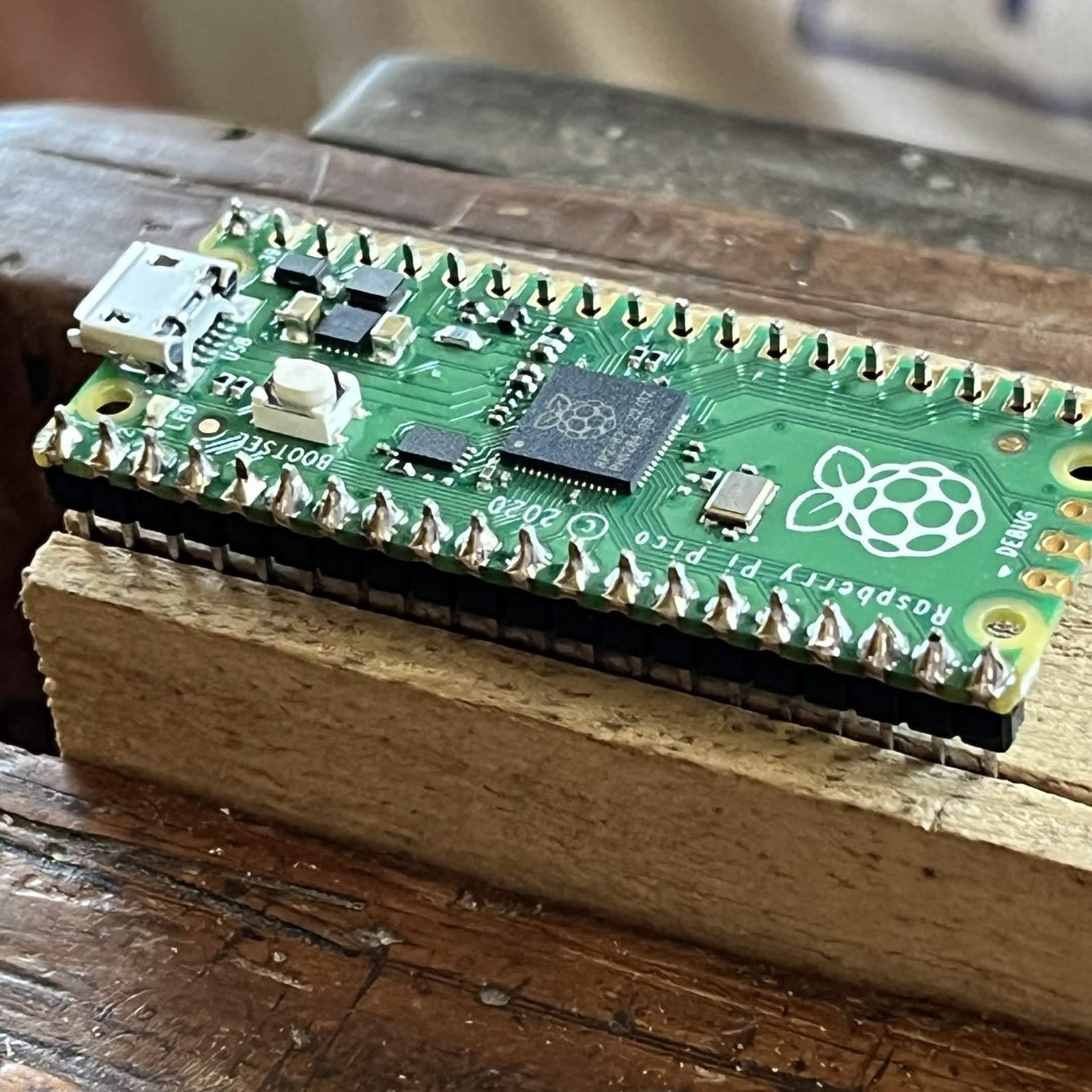 Close side view of the soldered Pico showing a solder fillet on every pad along the chip side and the black plastic of the header pressed flat against the underside of the board