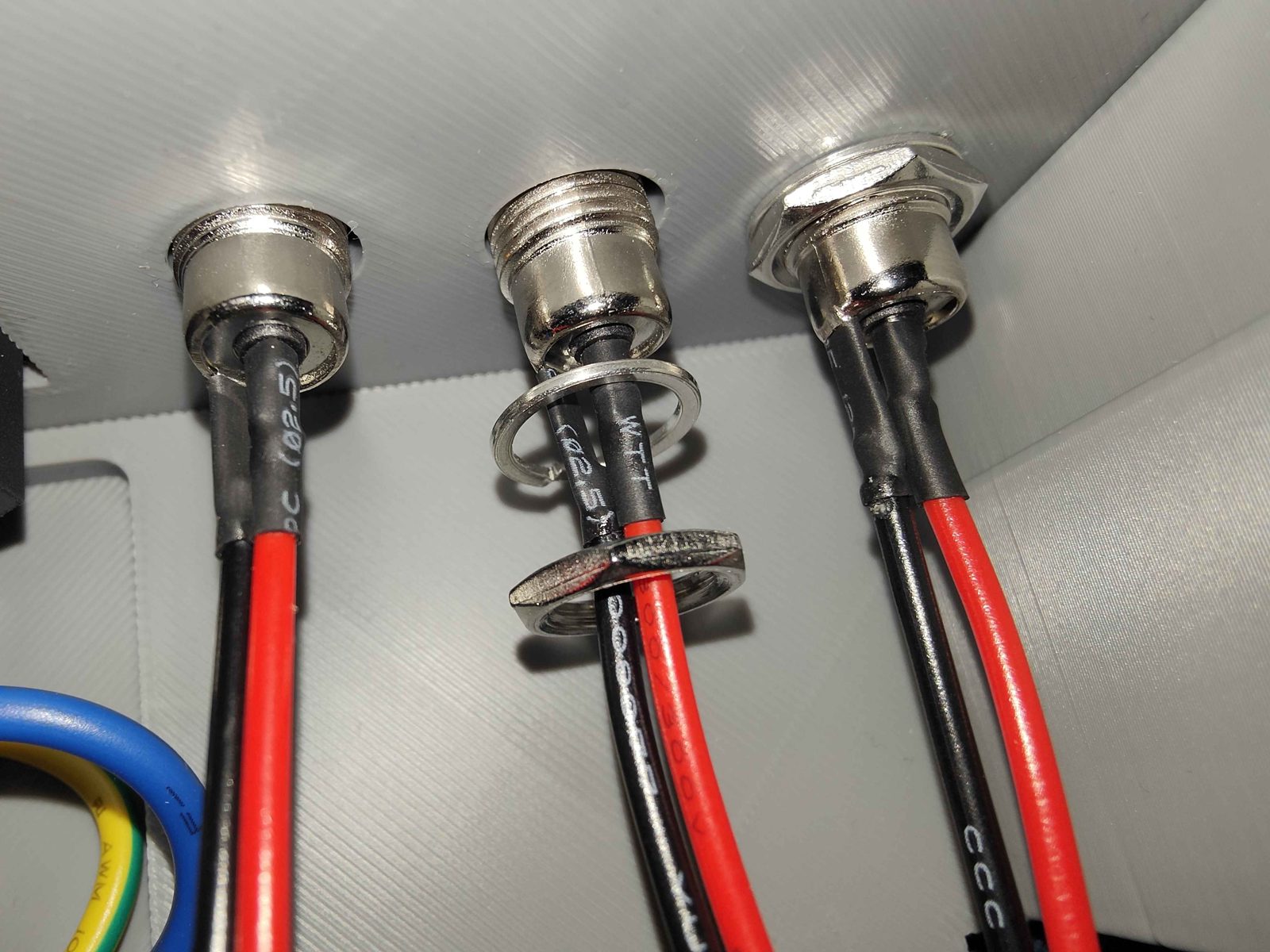 The inside of the front panel with three barrel jacks through it: the left jack bare, the middle one with its spring washer down on the thread and its nut still loose on the leads below, and the right one with the washer flattened under a tightened nut