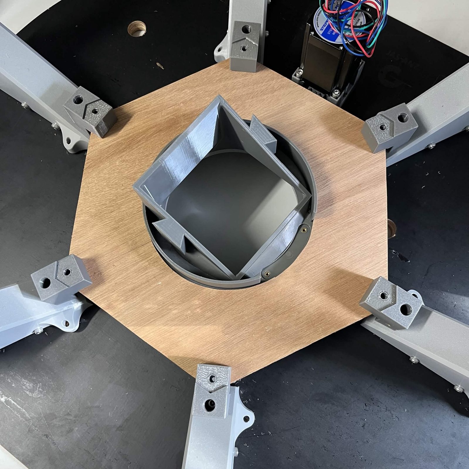 Looking down on the hexagonal plywood cage top slotted over the chute mount, the square mount standing through its centre hole and the printed brackets at the hexagon's corners