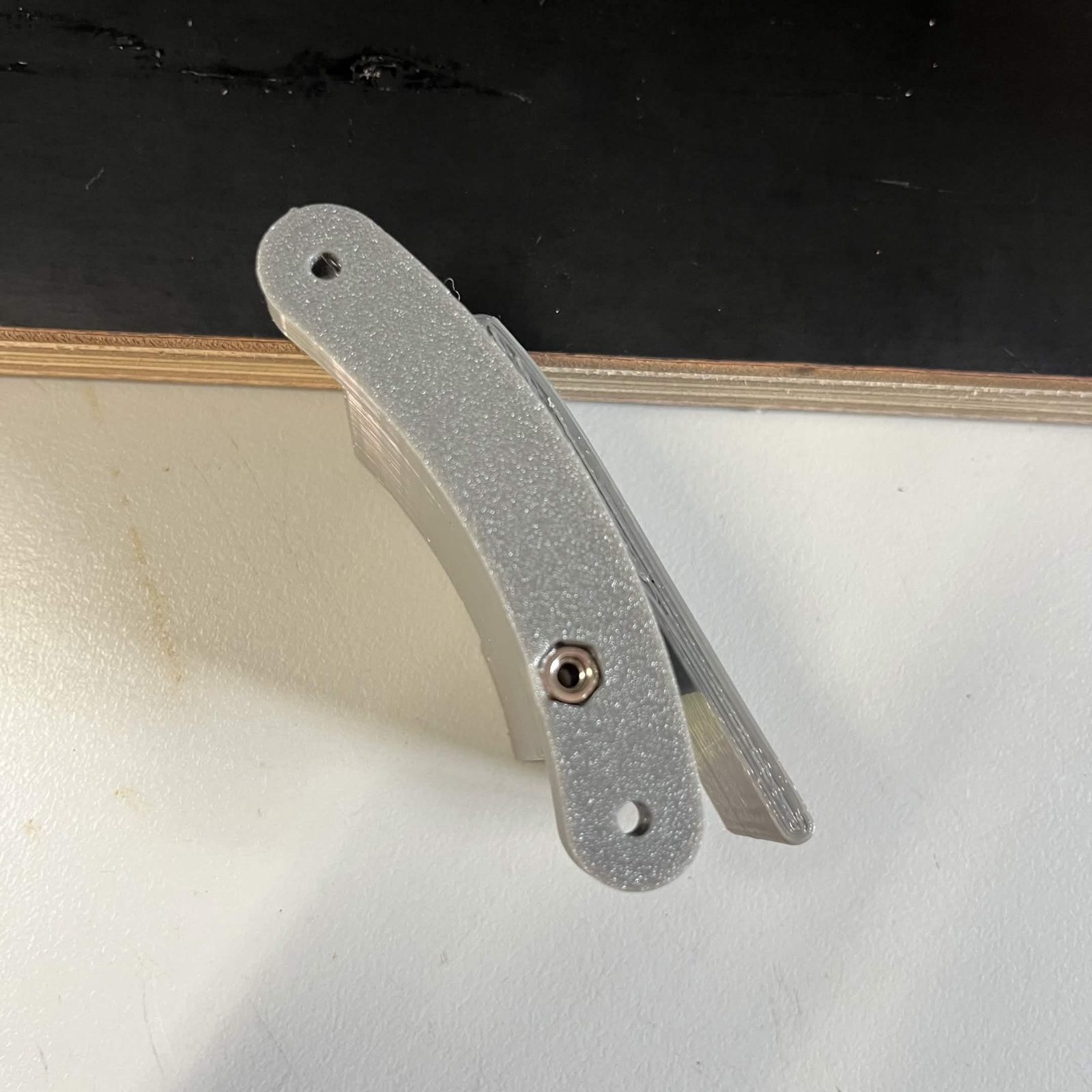 The curved ribbon cable clamp screwed to the post of the cable mount bracket with a single screw through its middle, no cable in it yet