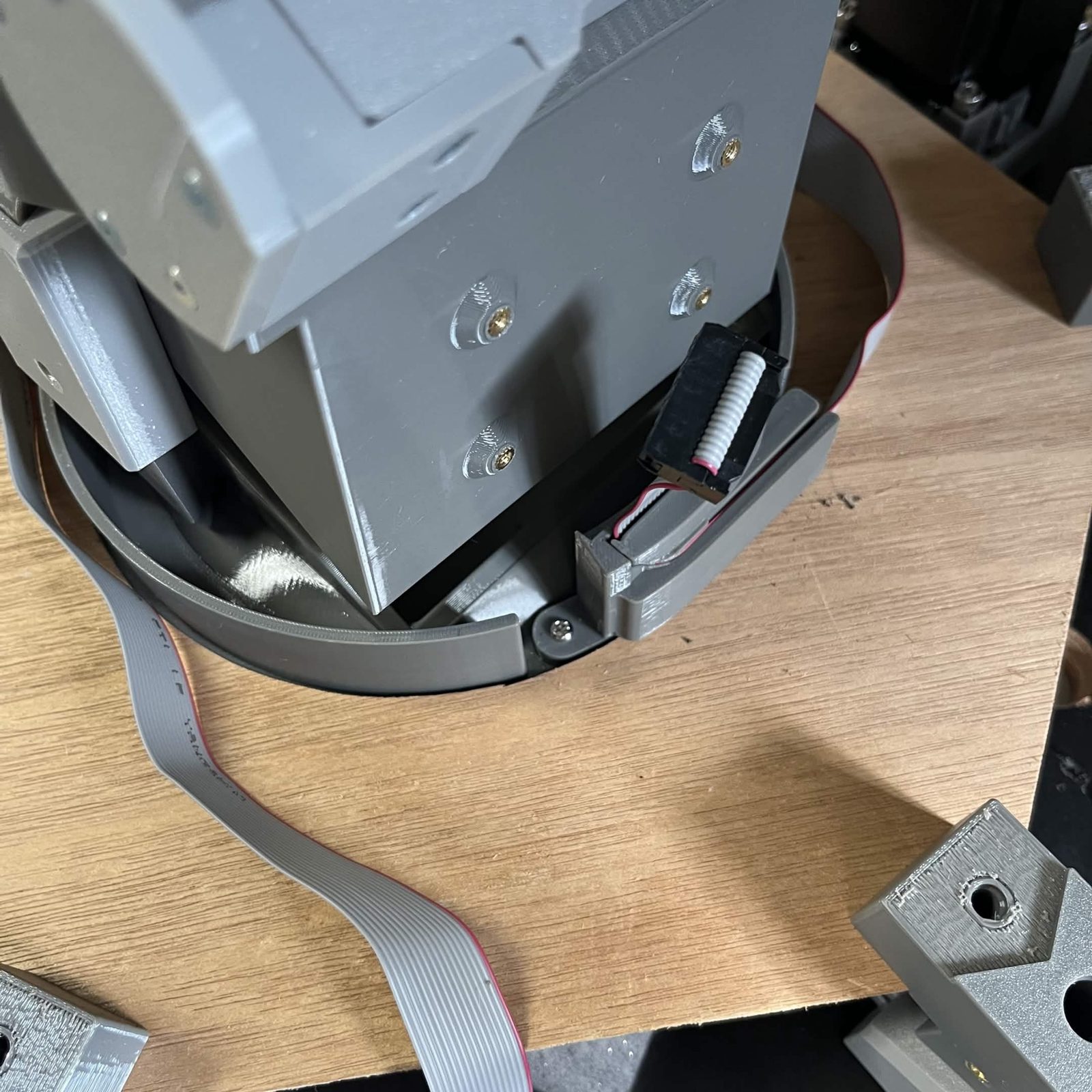 The ribbon cable brought up beside the chute mount with its IDC connector standing free, a loop of cable running down to the plywood, and four brass heat inserts in the face beside it